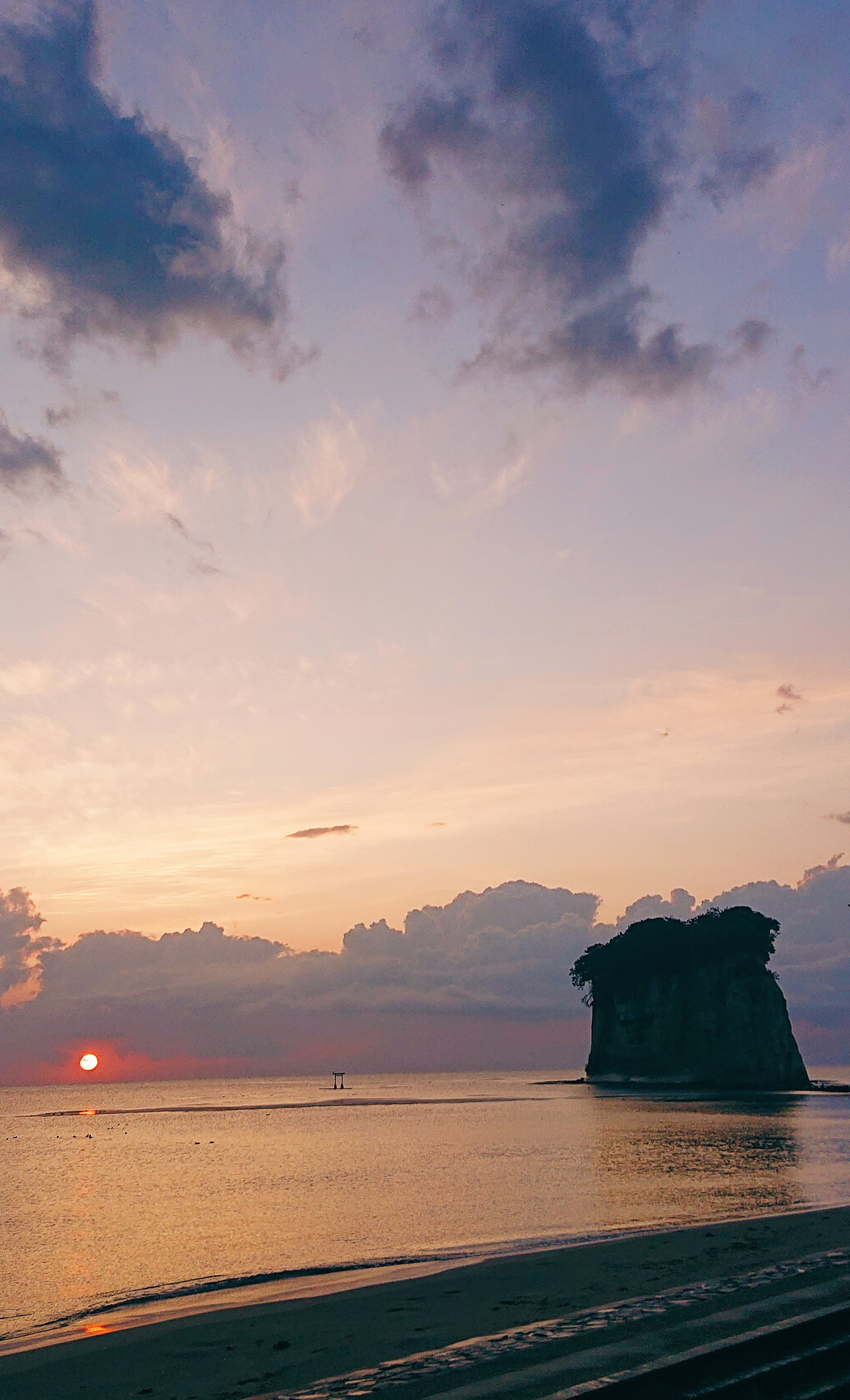 Coastal landscape at sunset featuring a large rock and beautiful cloud silhouettes