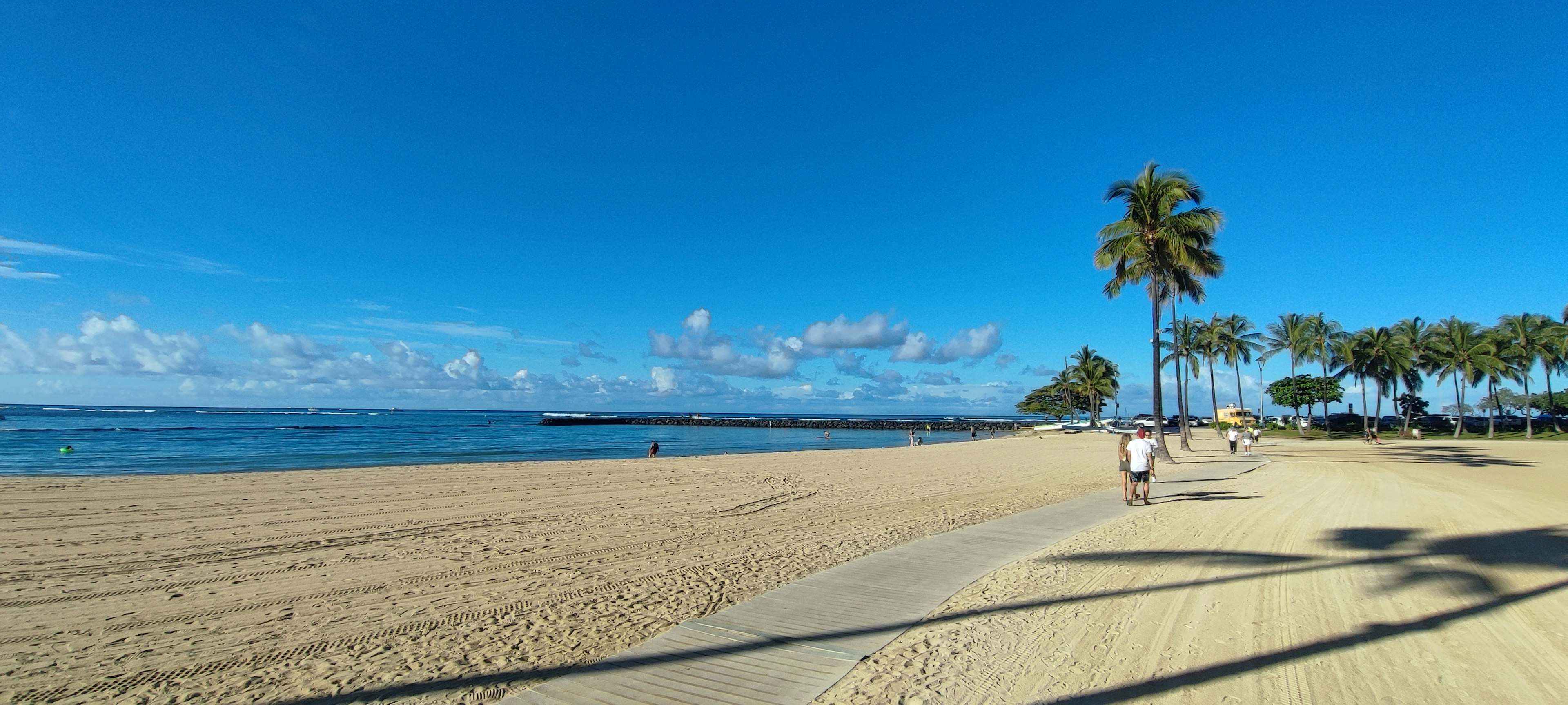 Menschen, die an einem Sandstrand mit Palmen und klarem blauen Himmel spazieren