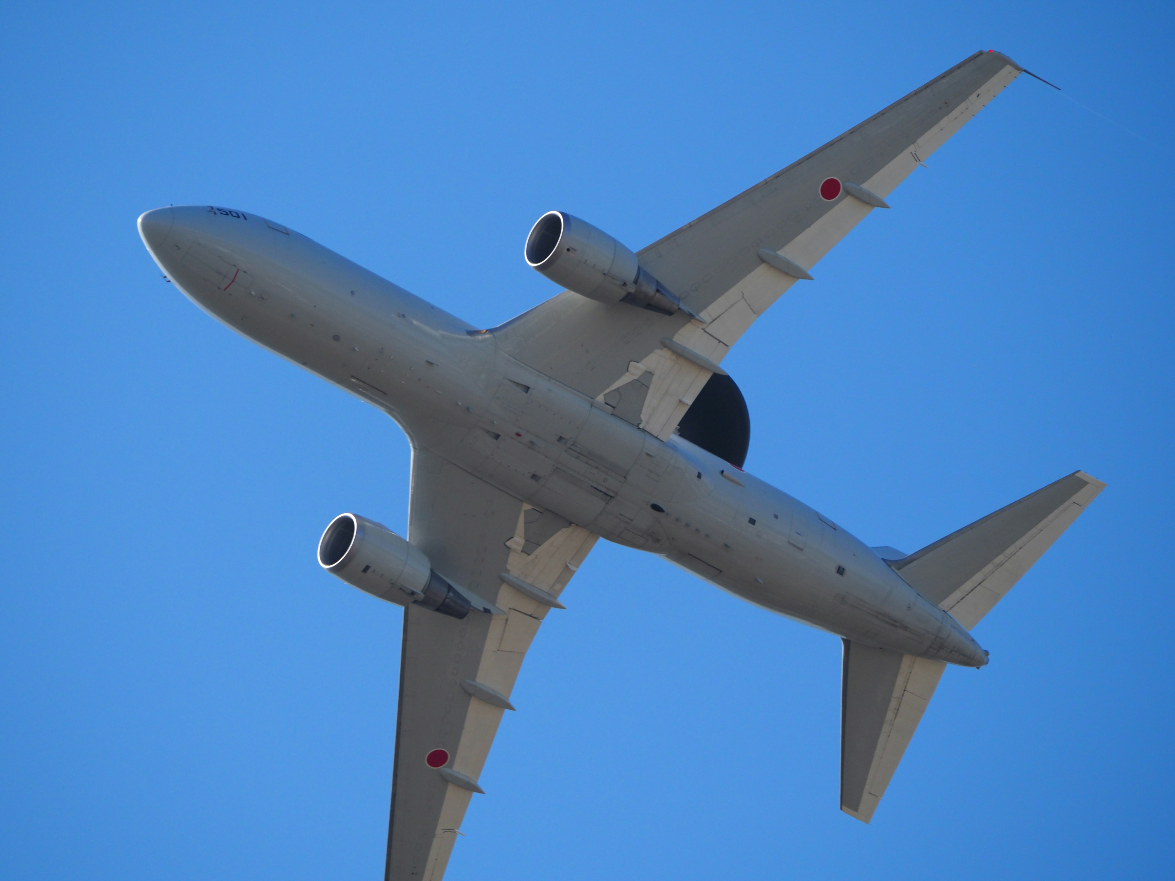 A jet airplane flying against a clear blue sky from below