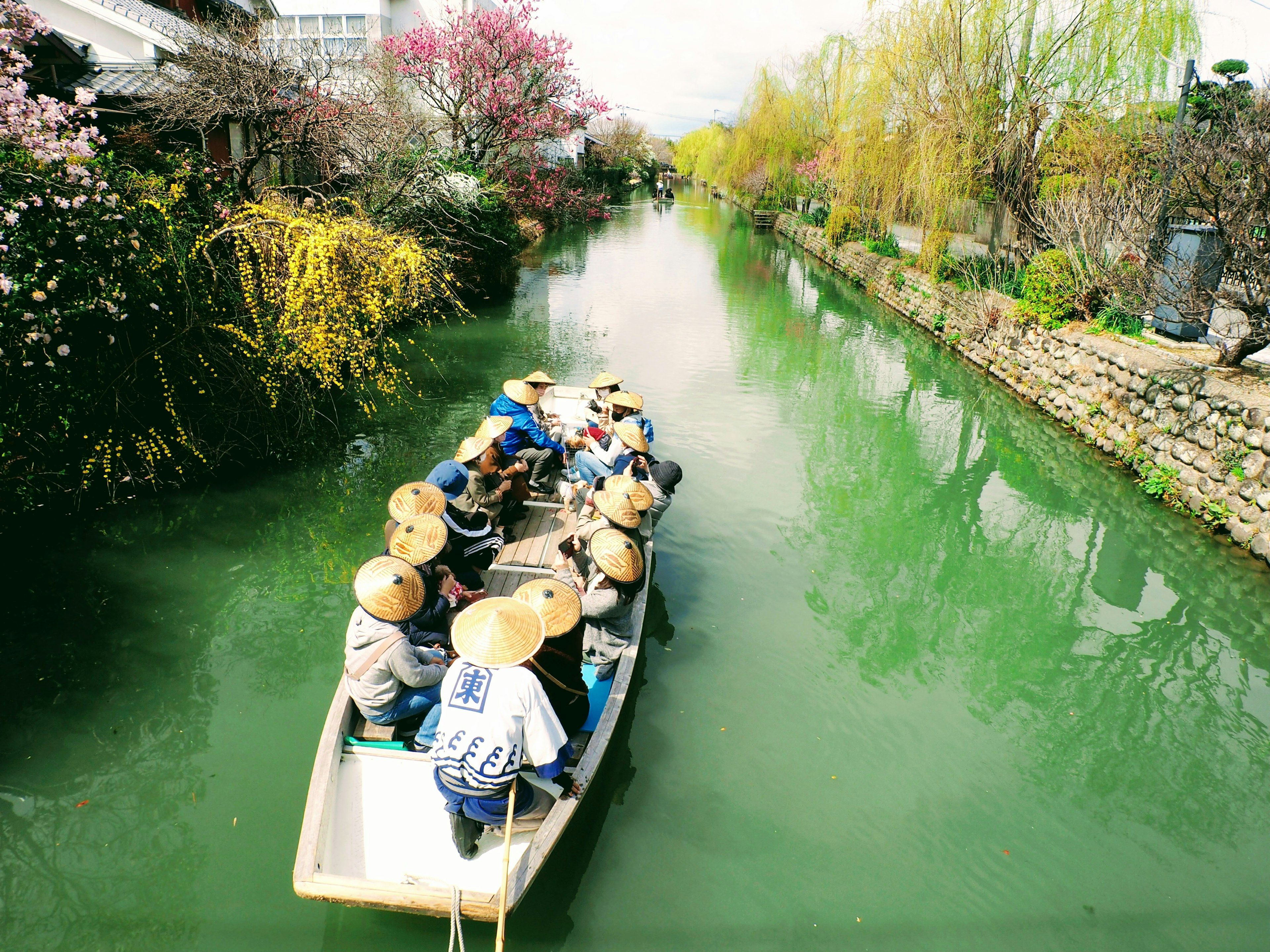 Menschen rudern auf einem grünen Fluss umgeben von bunten Blumen