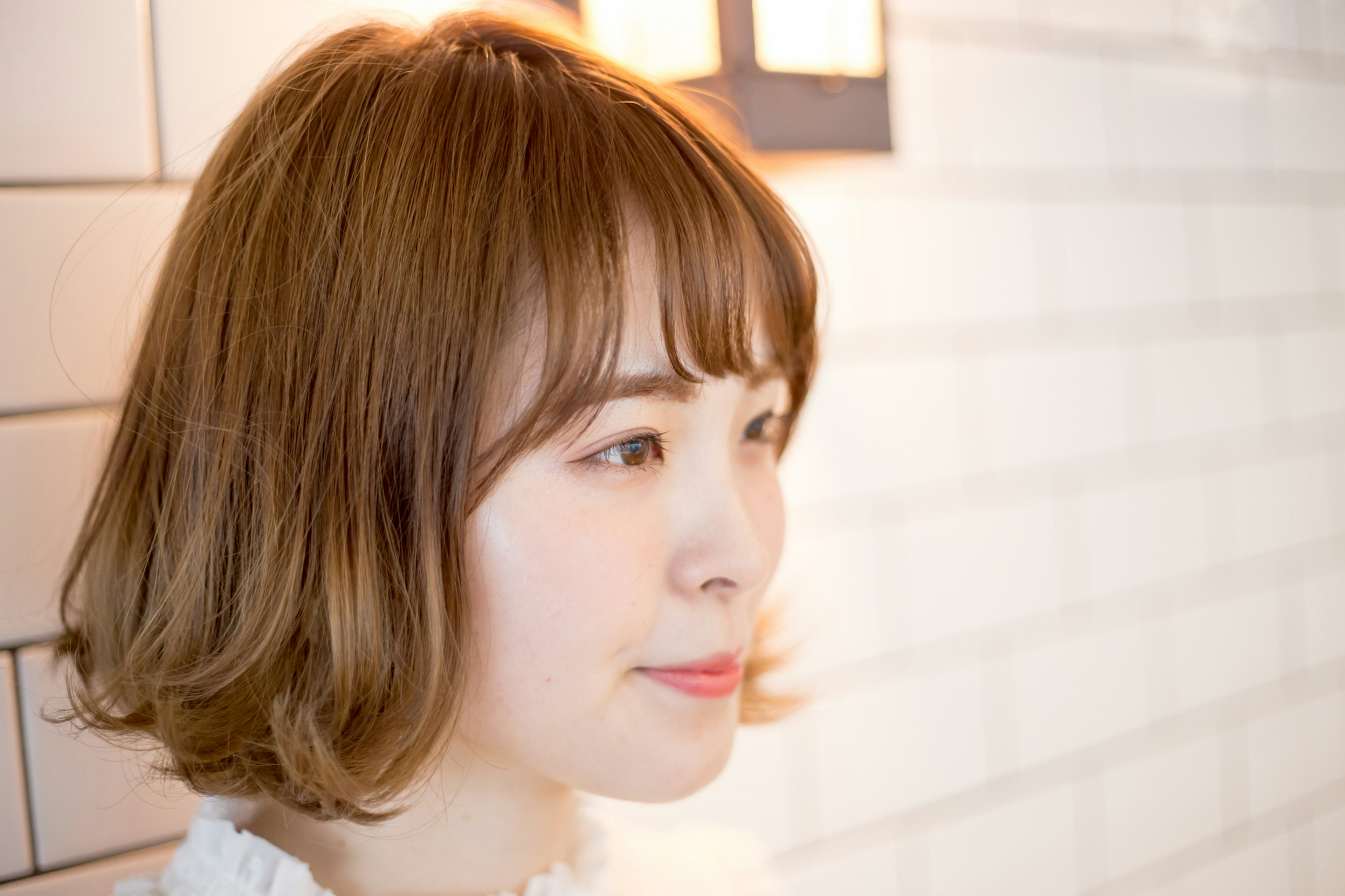 Profile of a young woman with light brown hair and a charming expression standing in front of a white wall