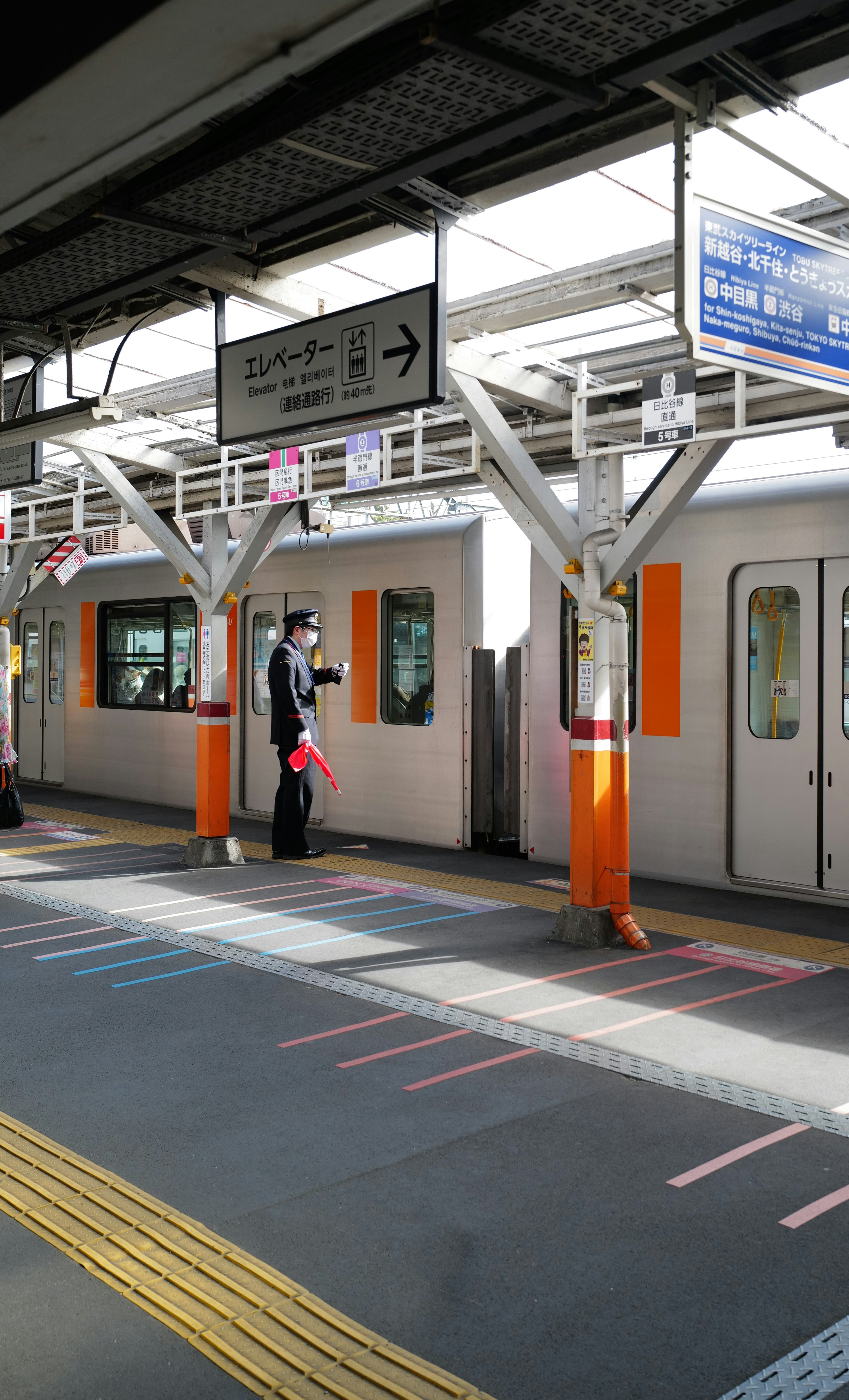 オレンジ色の車両が停車している駅のプラットフォームで、駅員が立っている風景