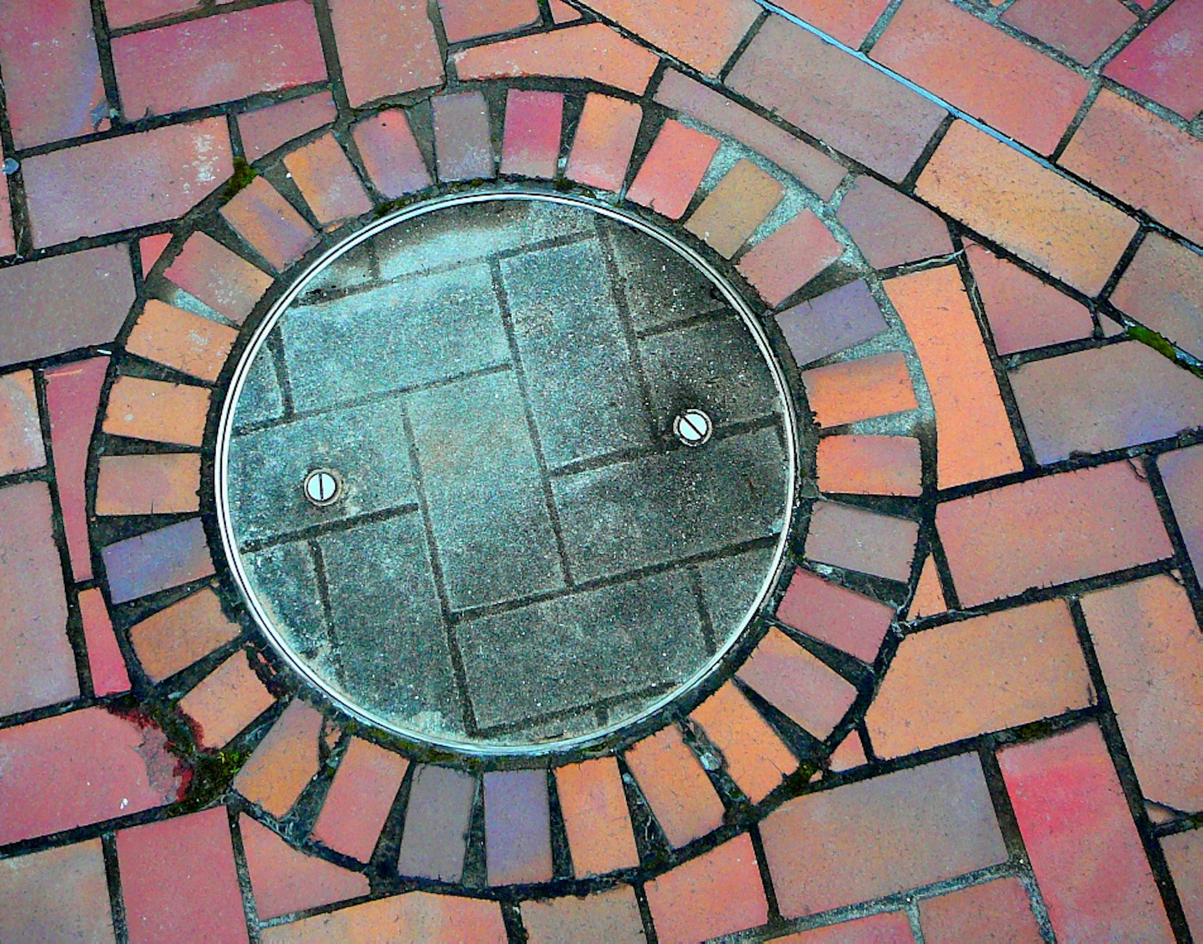 Manhole cover surrounded by colorful brick pavement