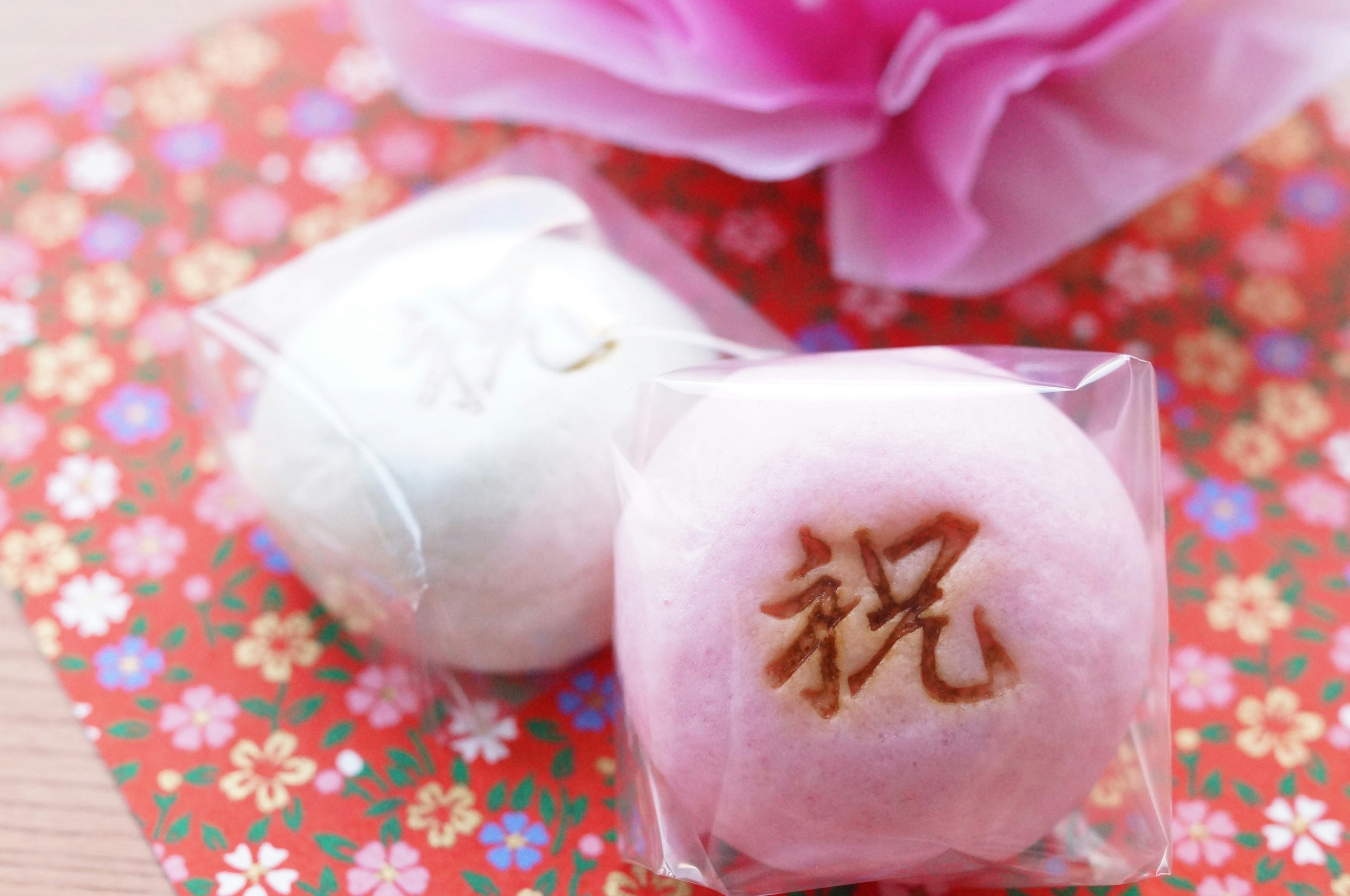 Two traditional Japanese sweets in white and pink on a floral patterned background