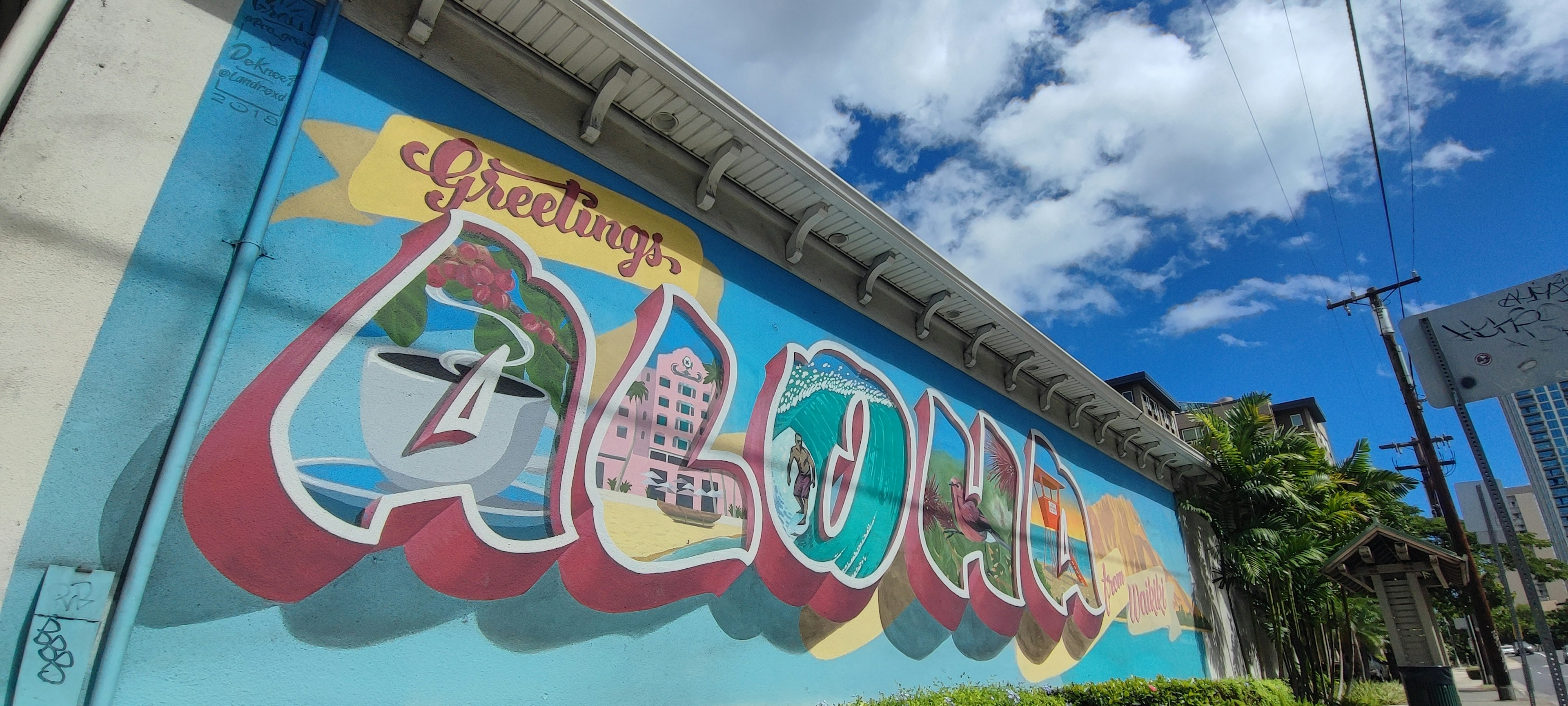 Mural ALOHA berwarna-warni dengan langit biru dan awan putih menangkap suasana Hawaii