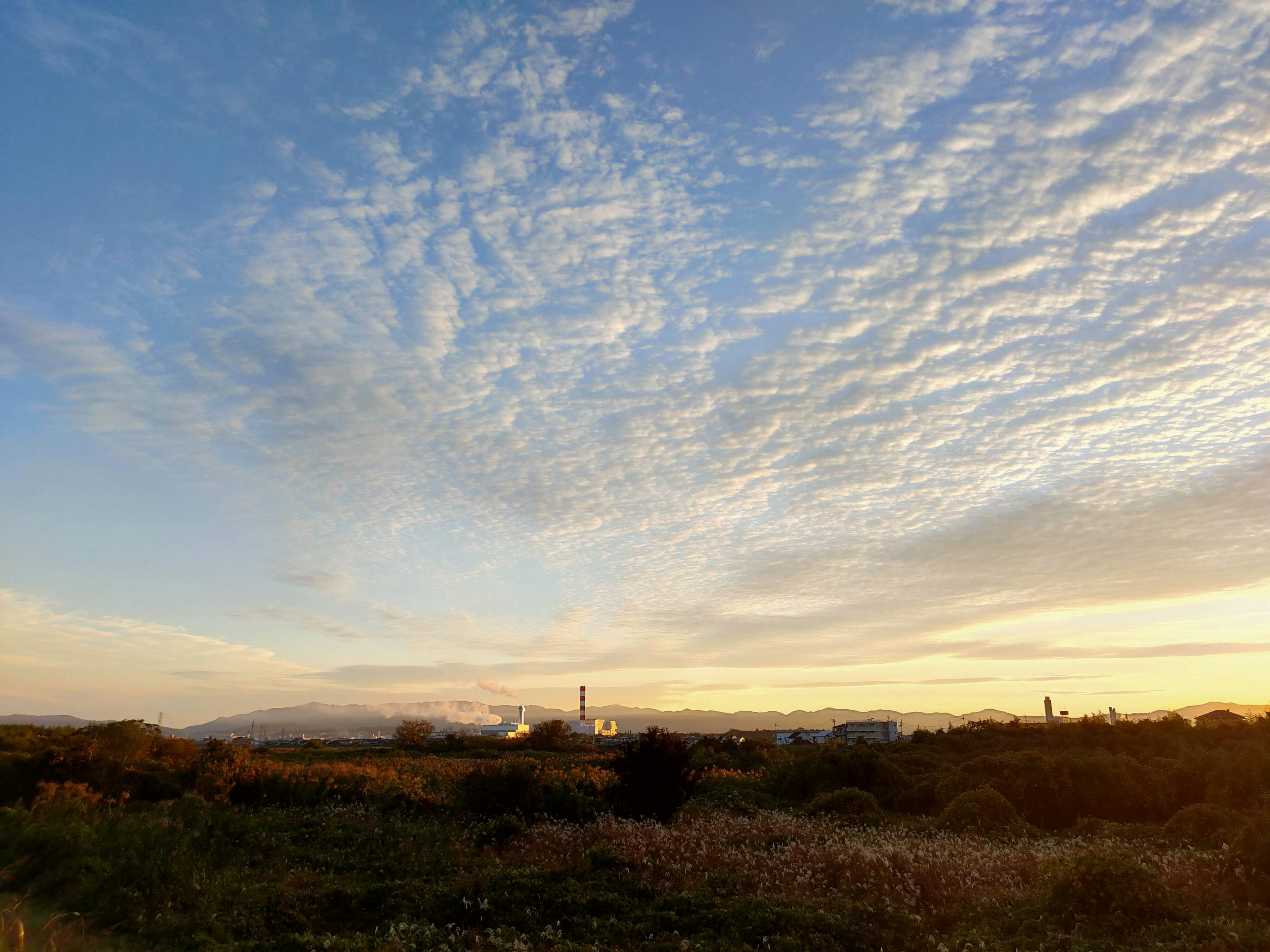 Landschaft mit blauem Himmel und Wolken mit industriellen Silhouetten