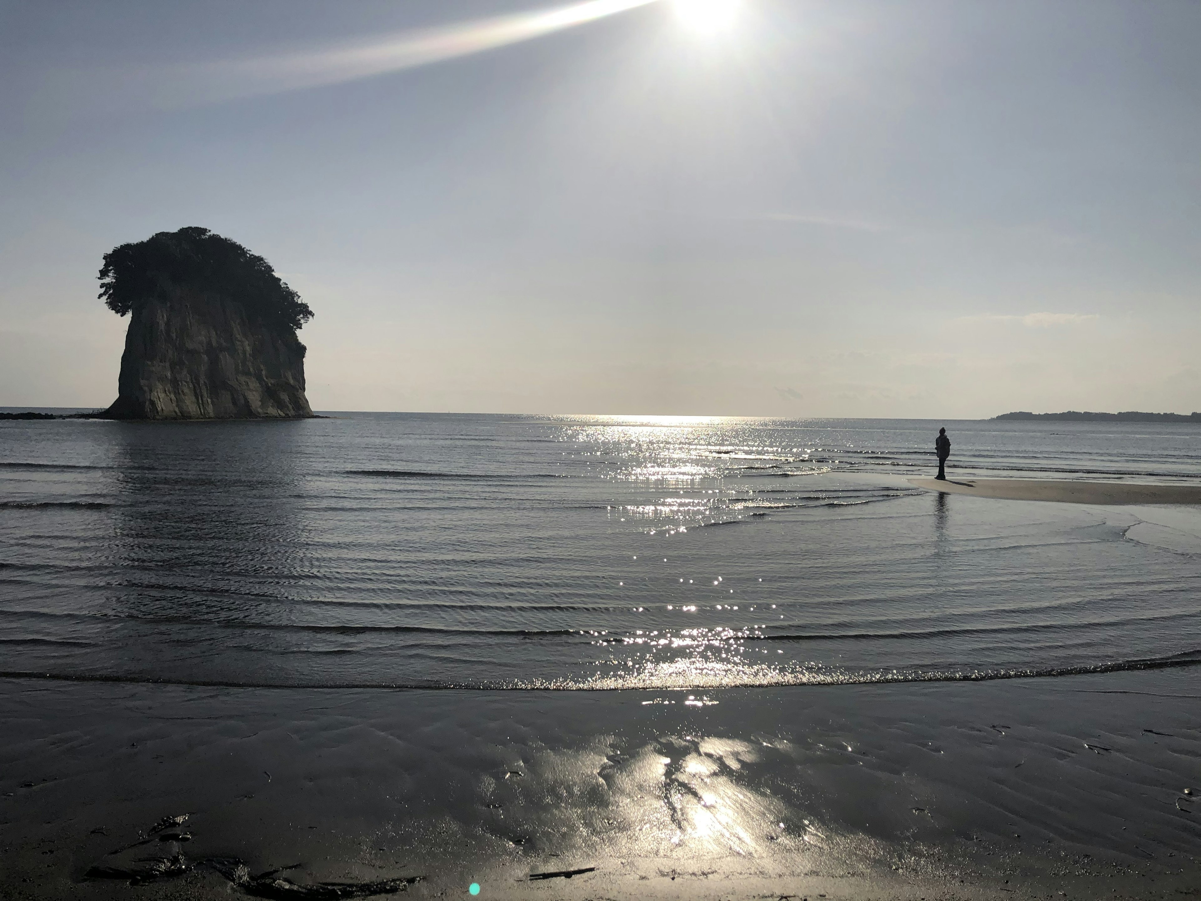 Una escena de playa serena con una figura solitaria y una gran formación rocosa