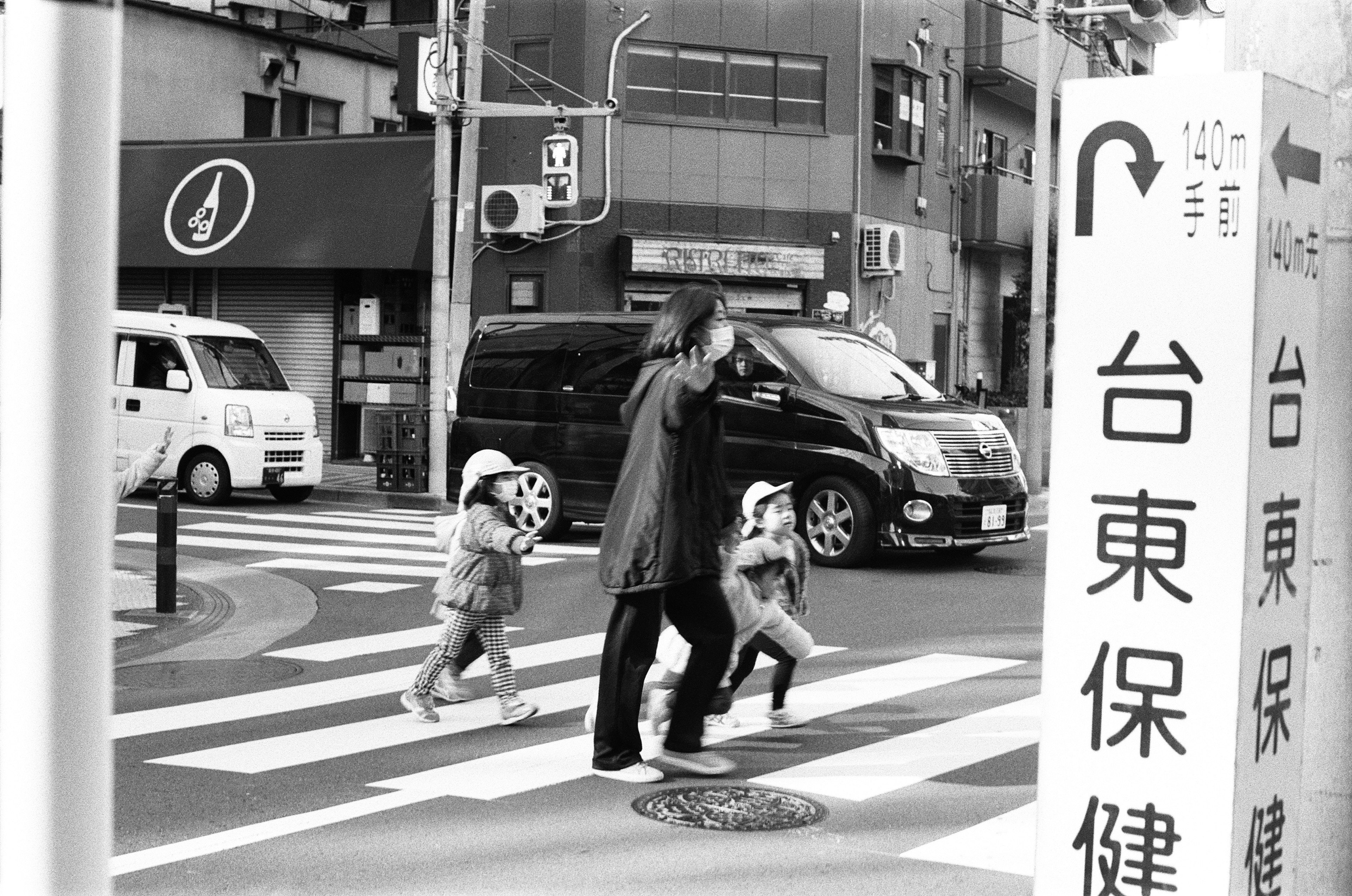 Un parent et deux enfants traversant un passage piéton dans une scène urbaine en noir et blanc