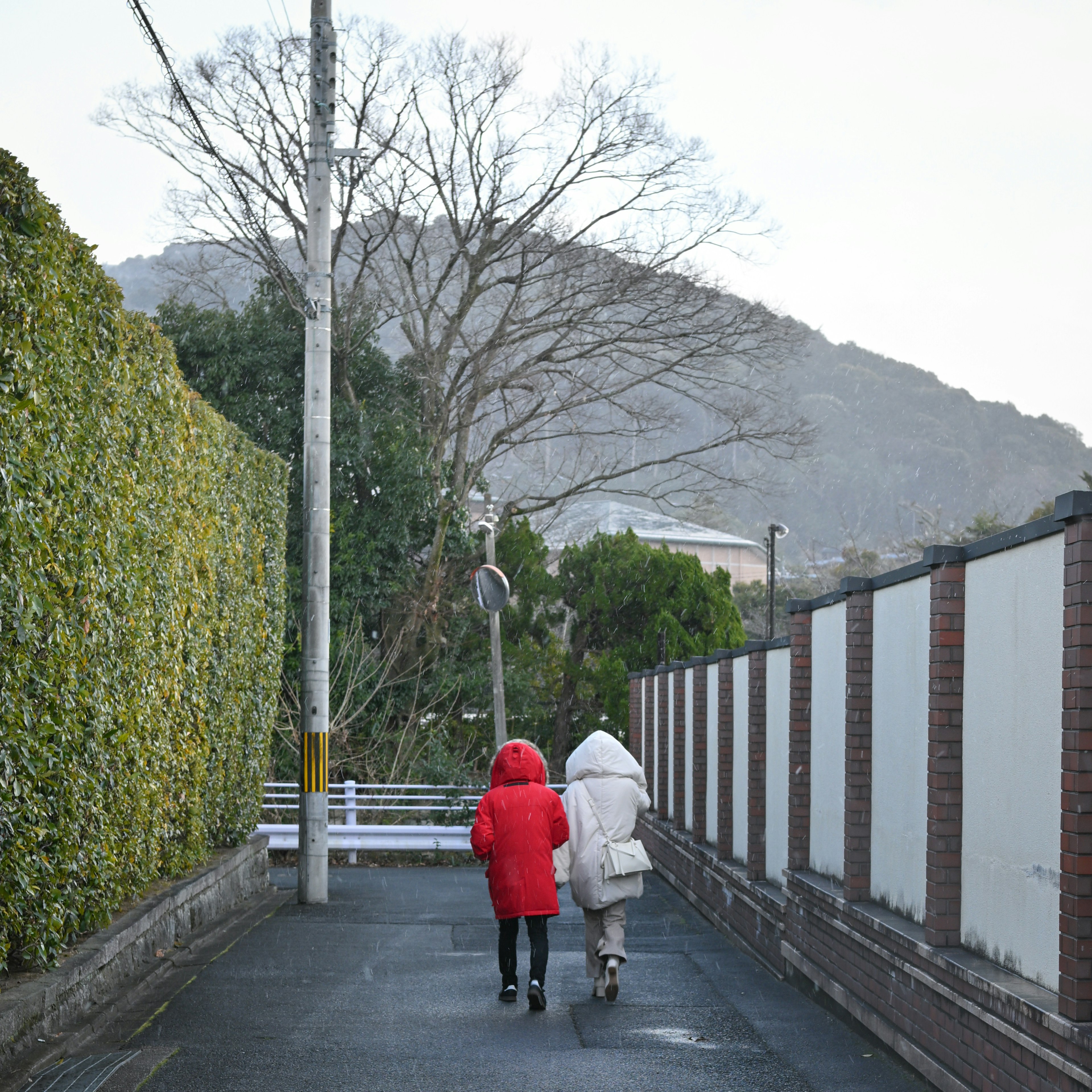 Dos figuras con abrigos rojo y blanco caminando por un sendero estrecho cerca de una montaña