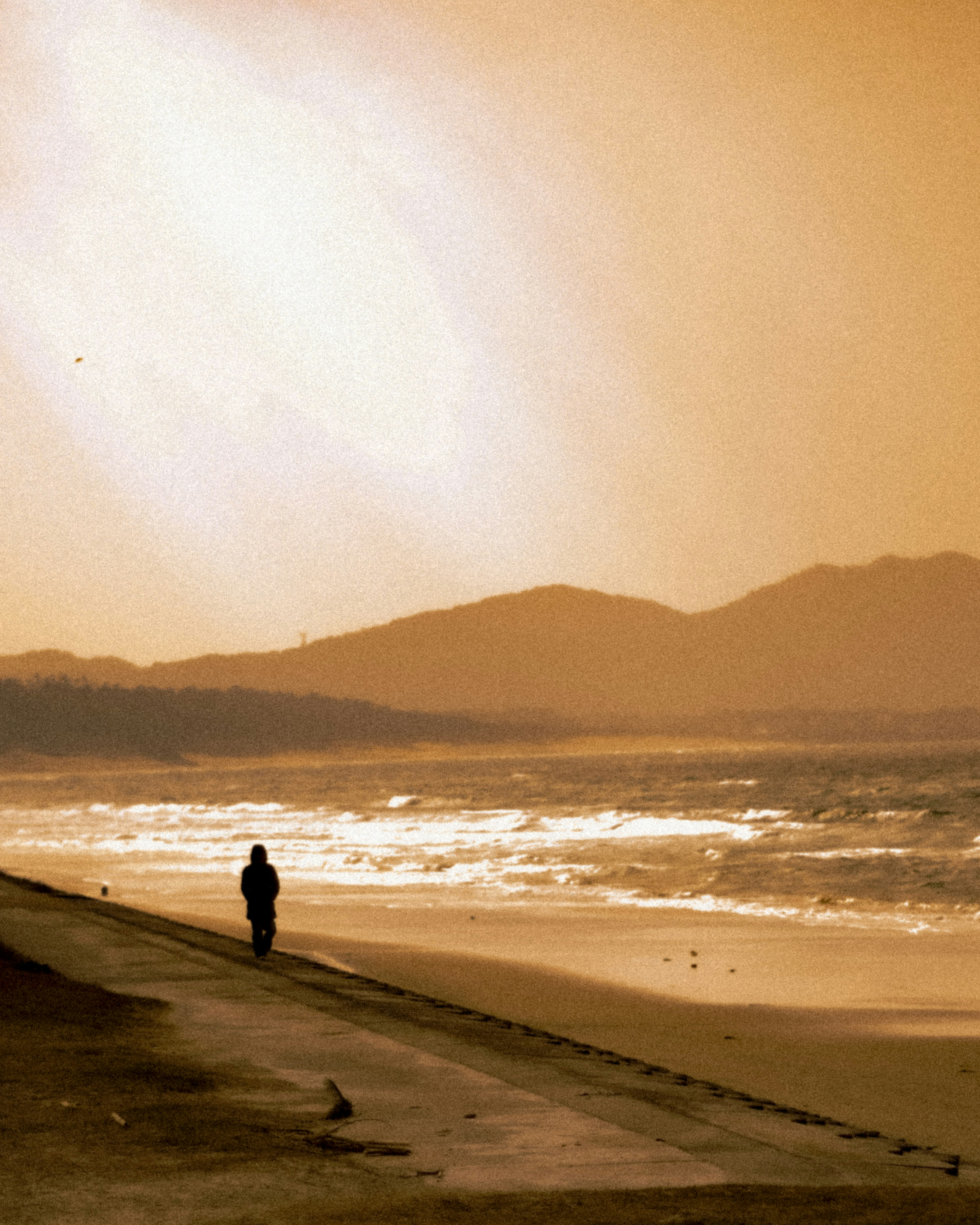 Silhouette di una persona che cammina sulla spiaggia con montagne al tramonto