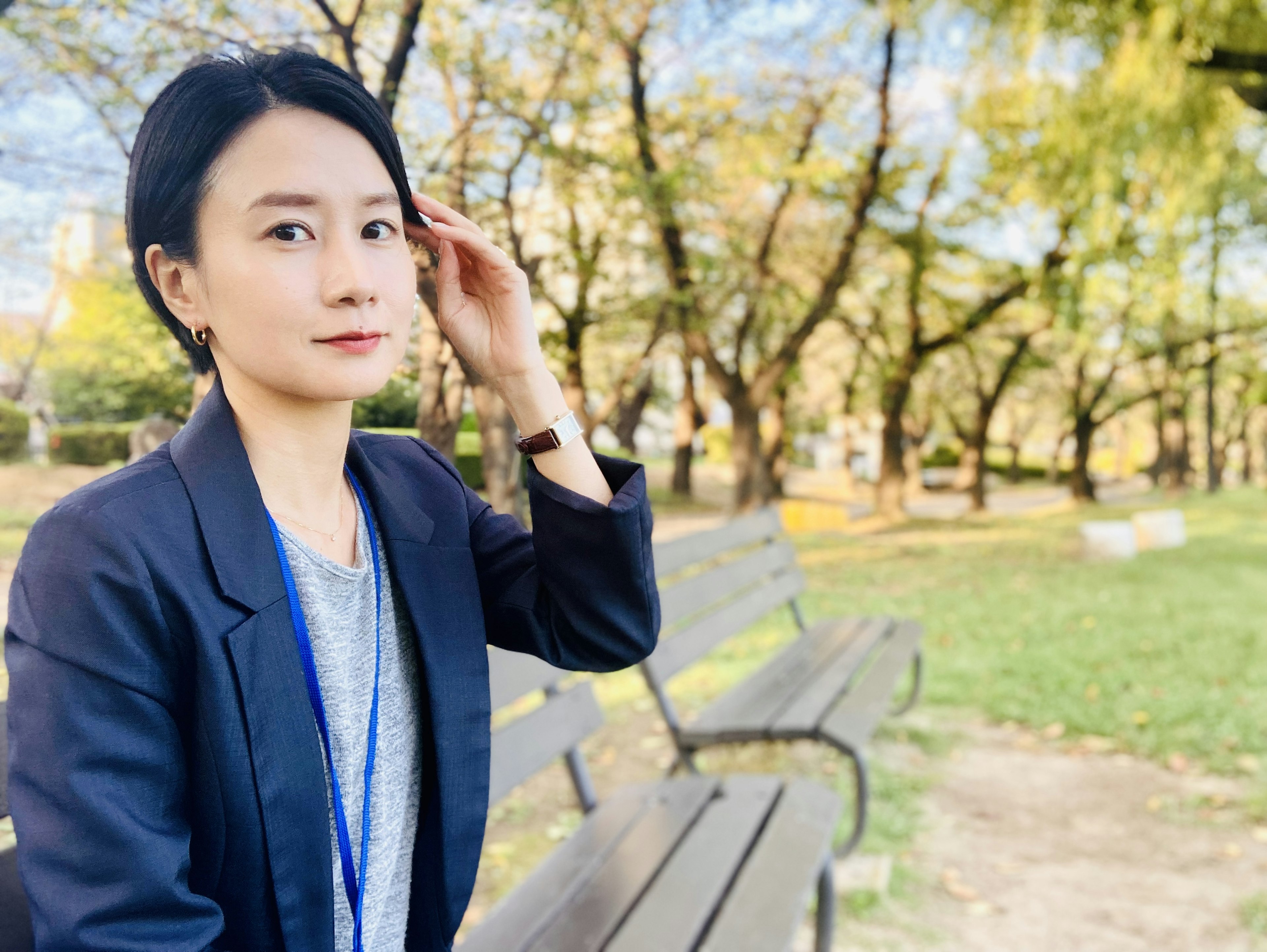 Retrato de una mujer sentada en un banco de parque rodeada de árboles de otoño vistiendo ropa casual y una chaqueta de negocios