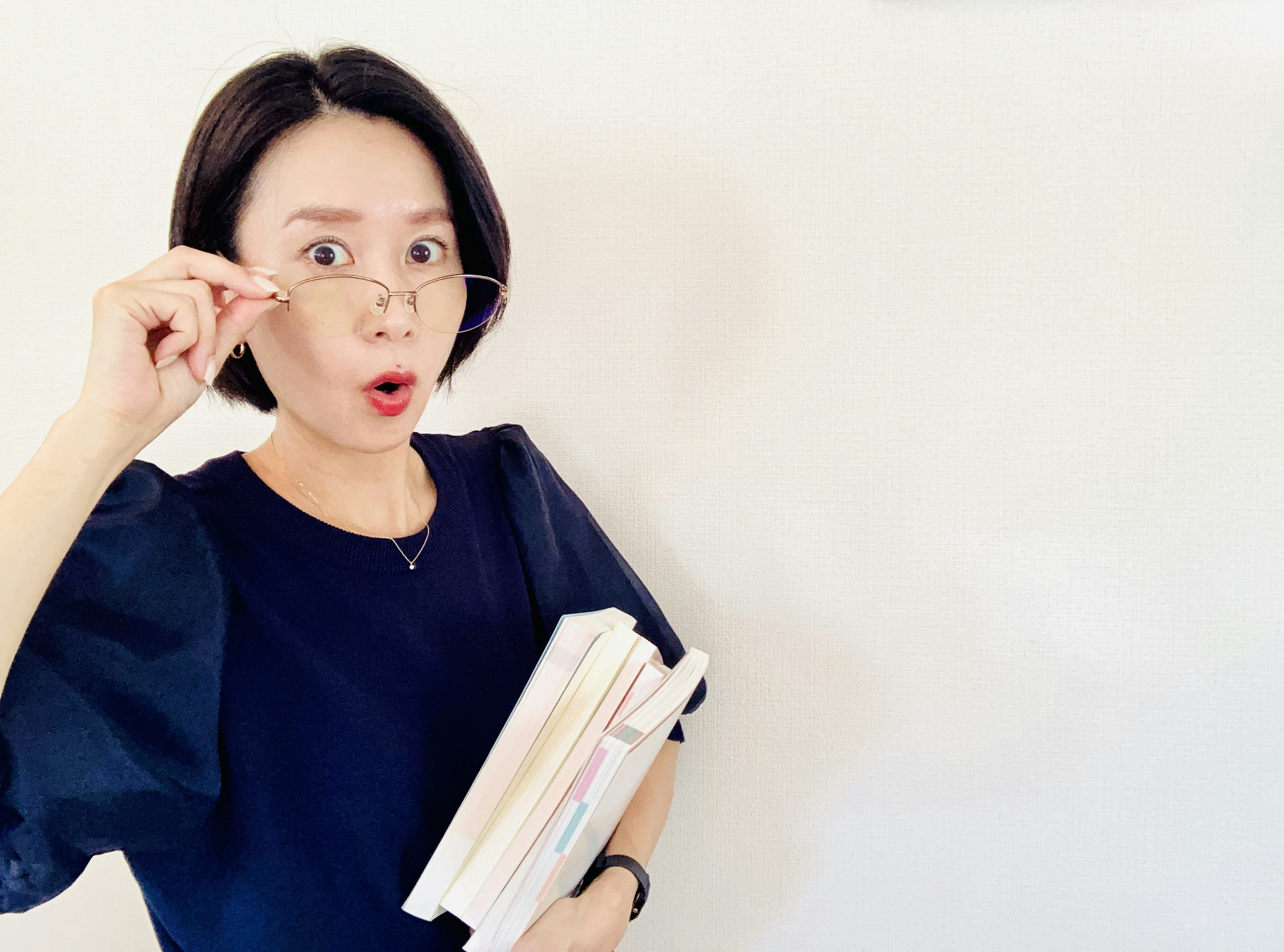 Woman holding books with surprised expression wearing glasses