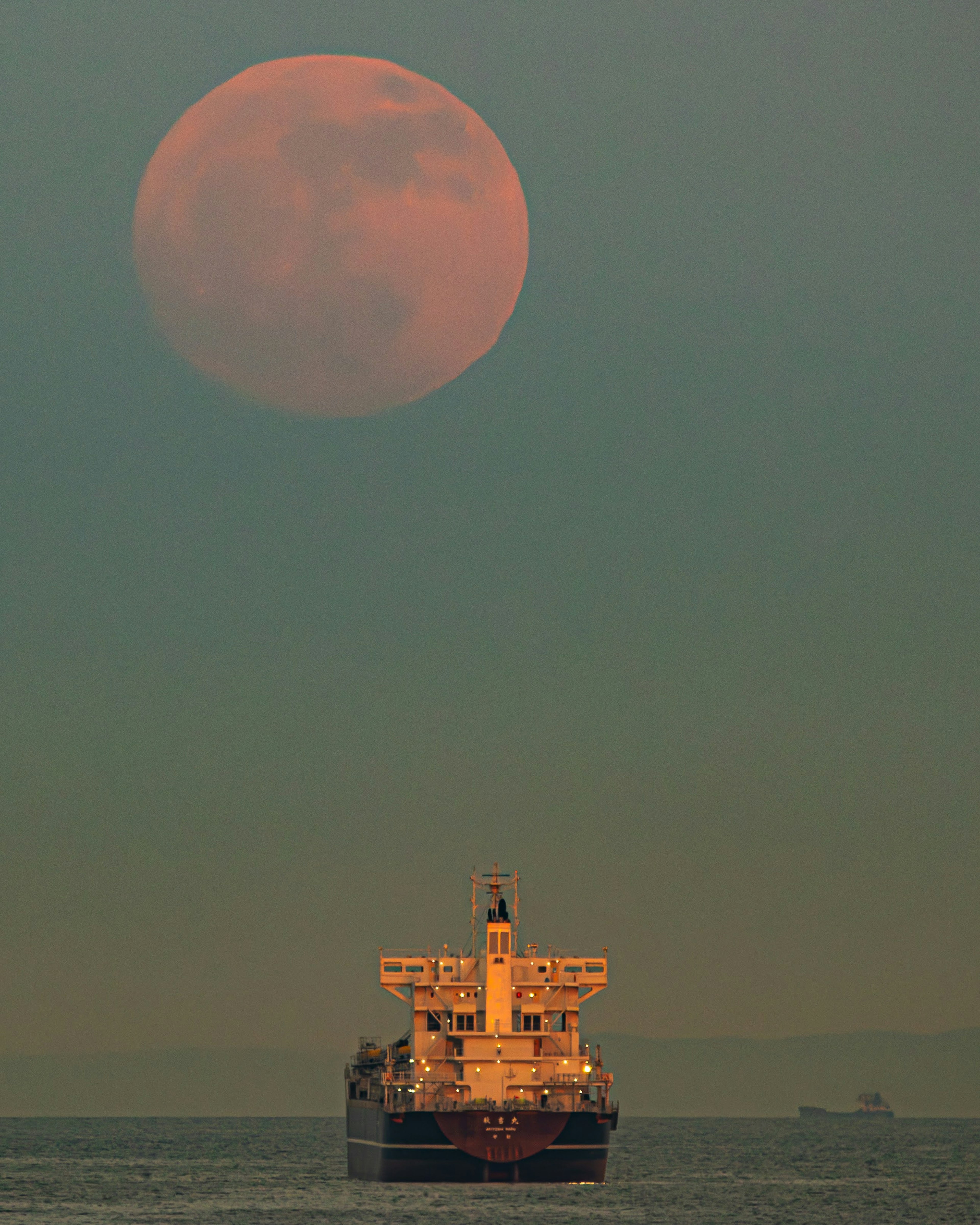 A ship silhouetted against a large full moon over the ocean