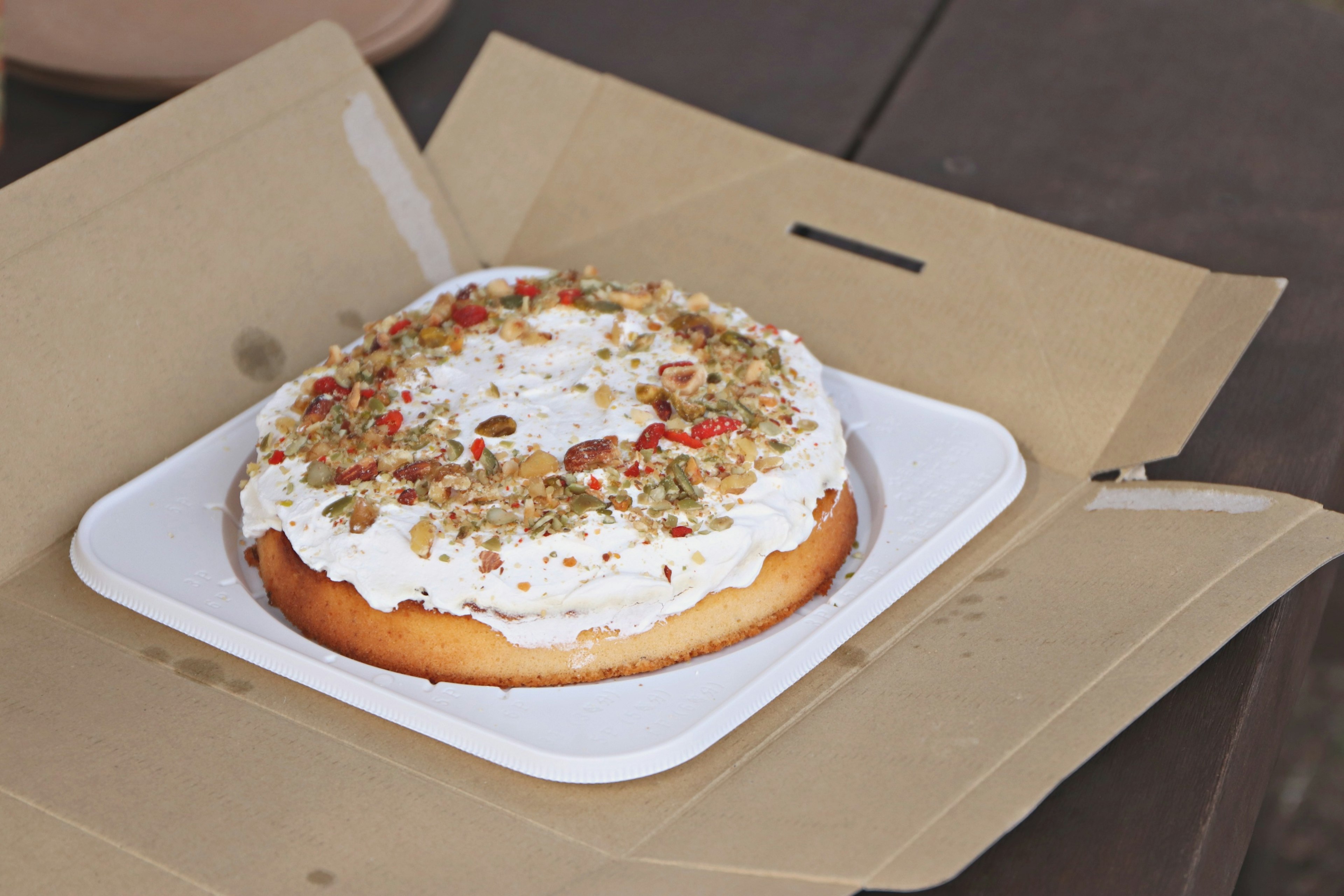 A cake topped with cream and garnished with nuts sits on a white plate