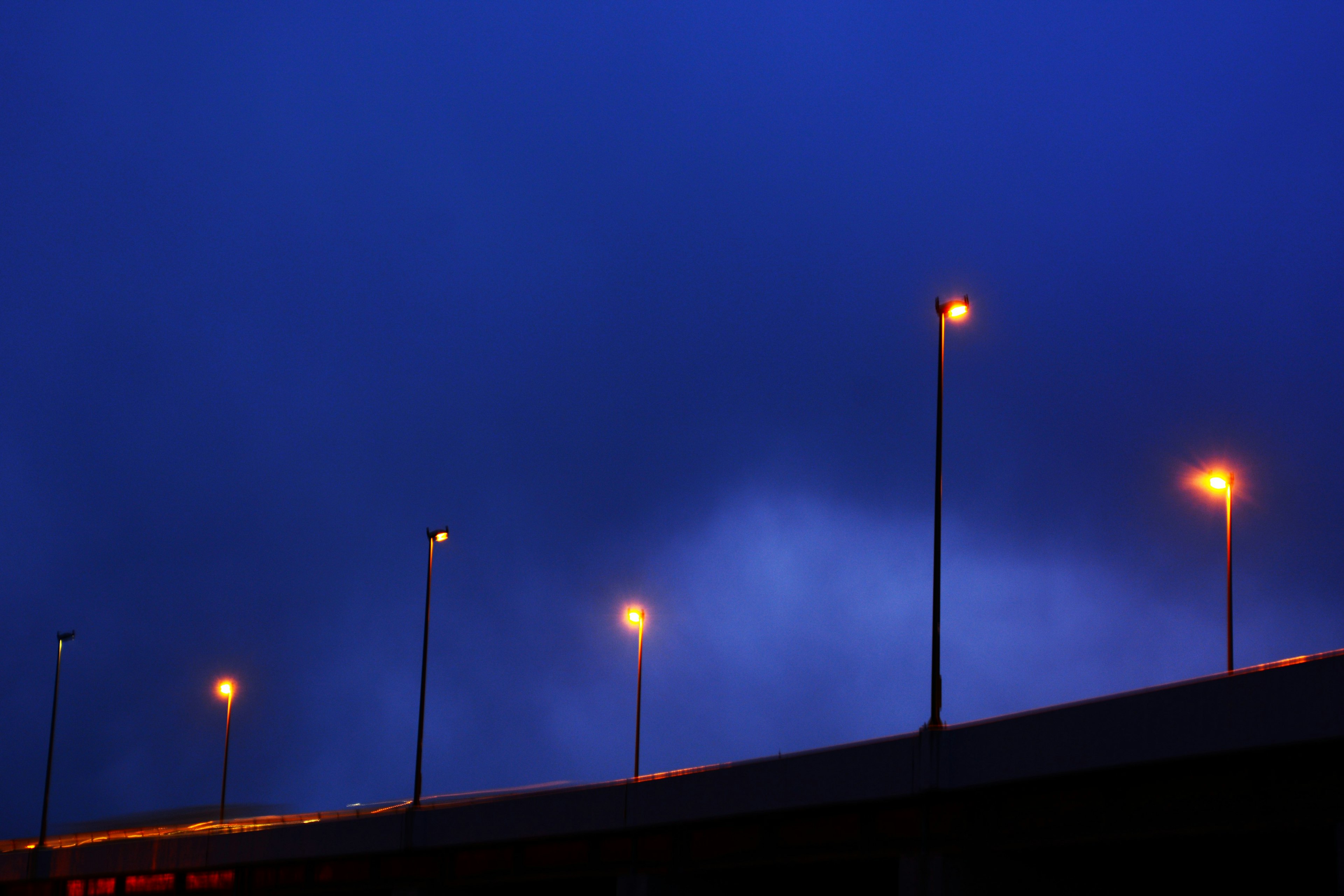 Silhouette of a bridge with streetlights under a blue sky