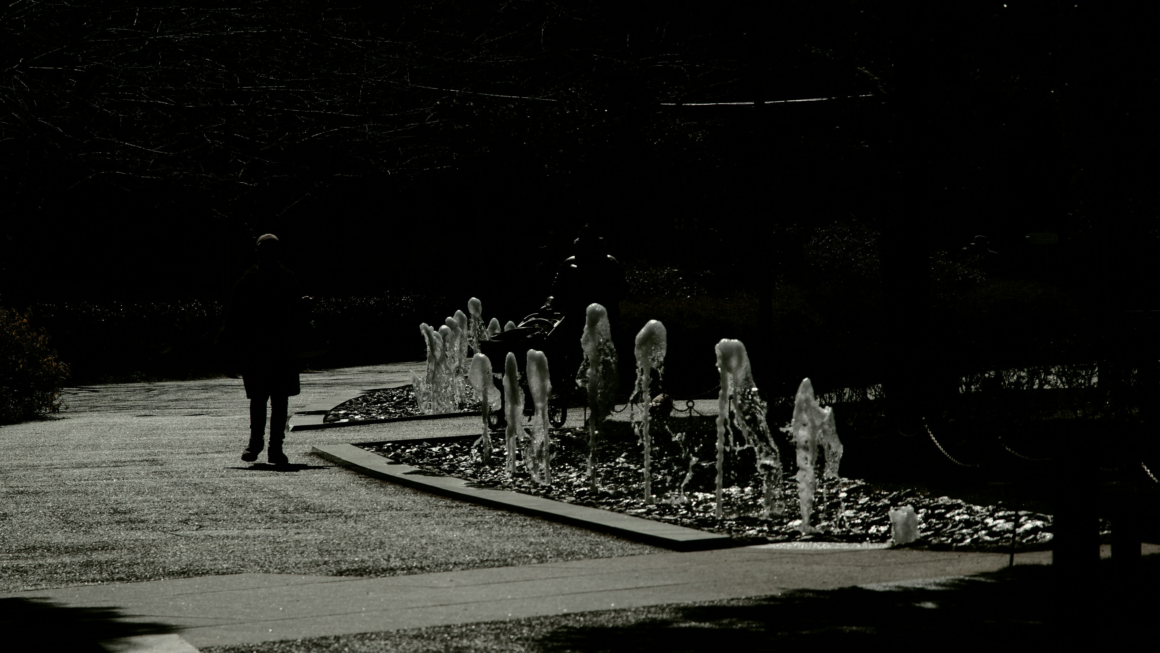 Una persona caminando por un sendero con esculturas en un parque en blanco y negro