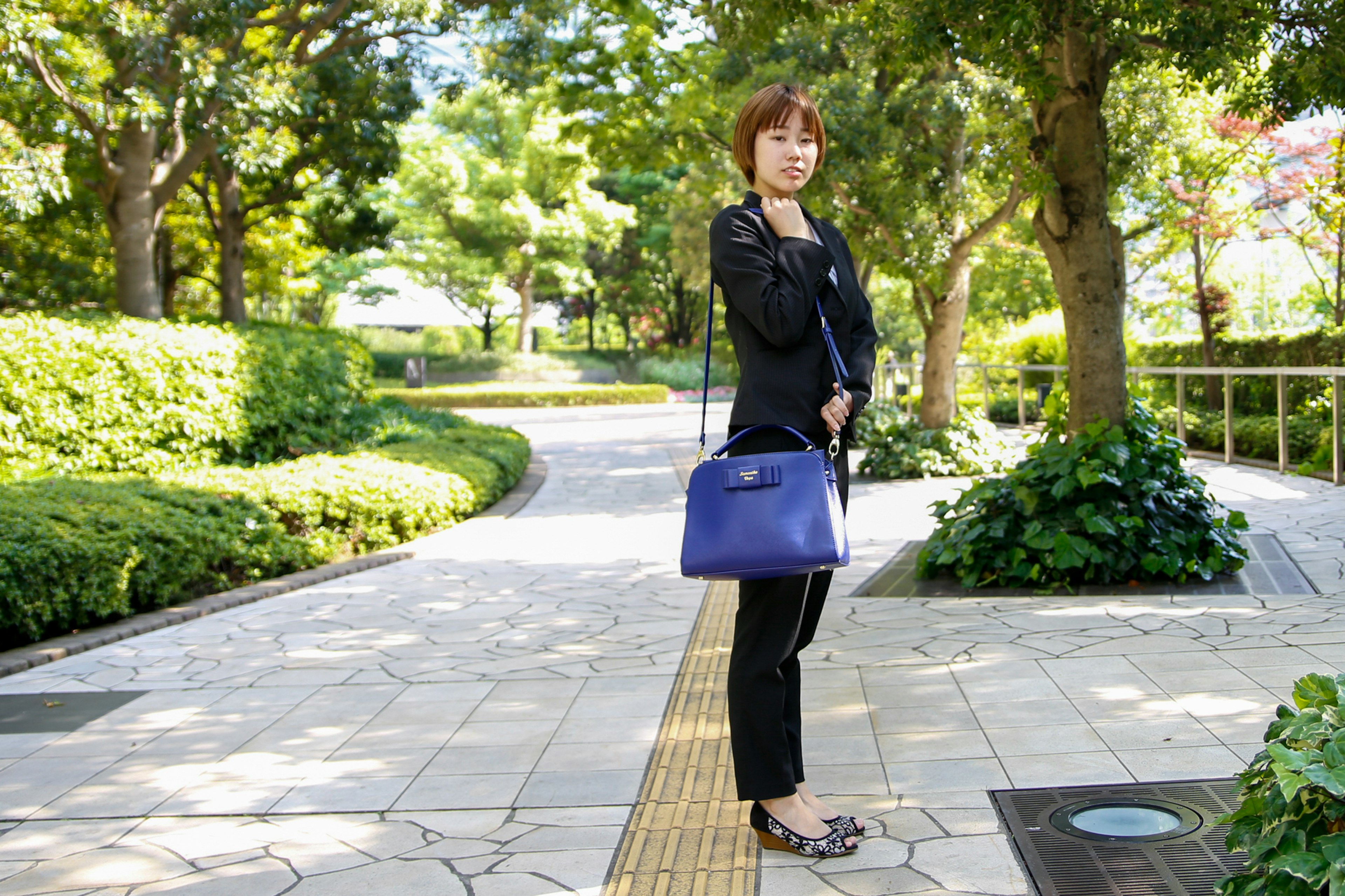 公園の小道で立っている女性 黒のジャケットを着ており 青いバッグを持っている