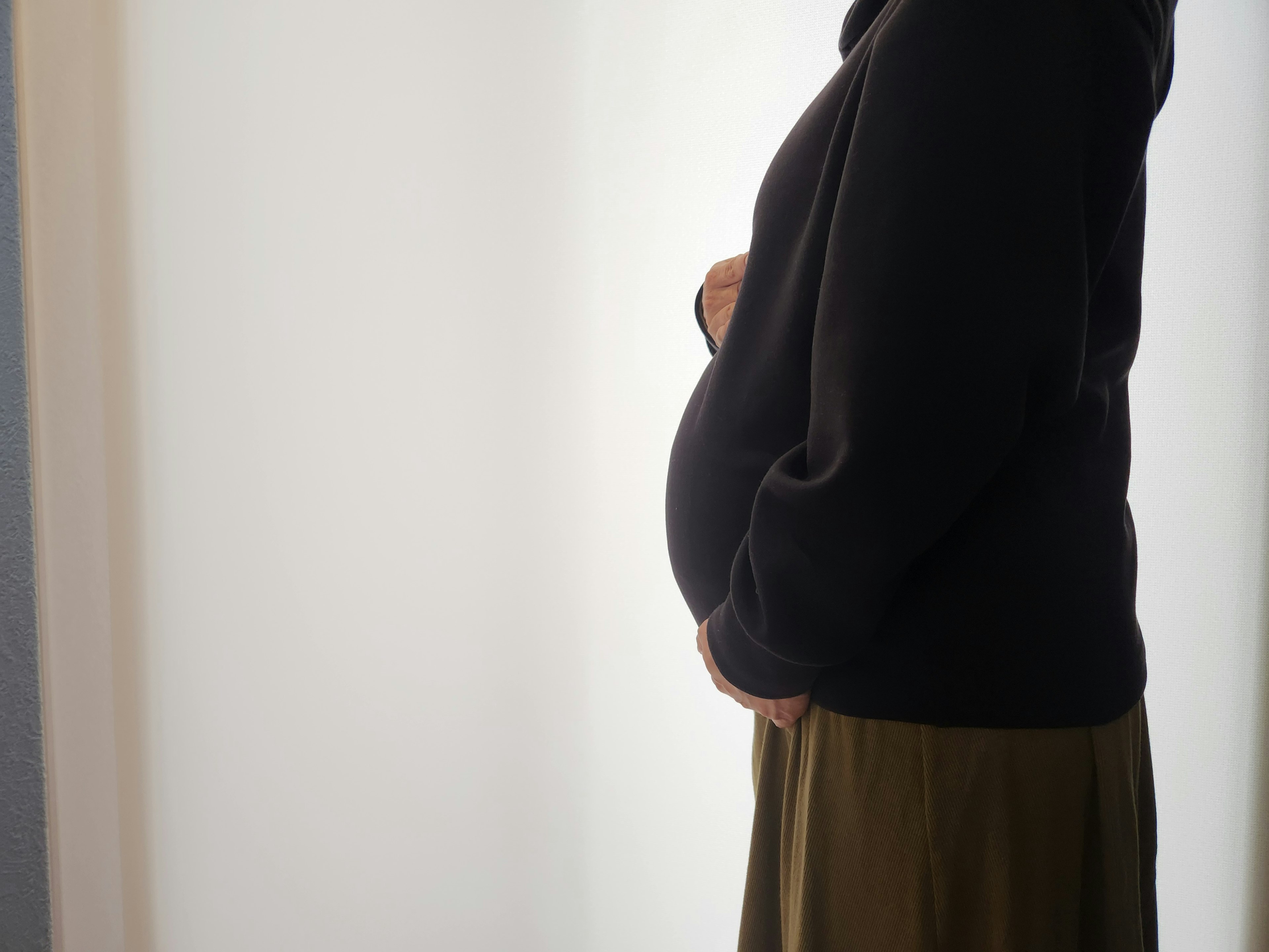 Seitenansicht einer schwangeren Frau Heller Hintergrund Schwarzer Pullover Grüne Rock