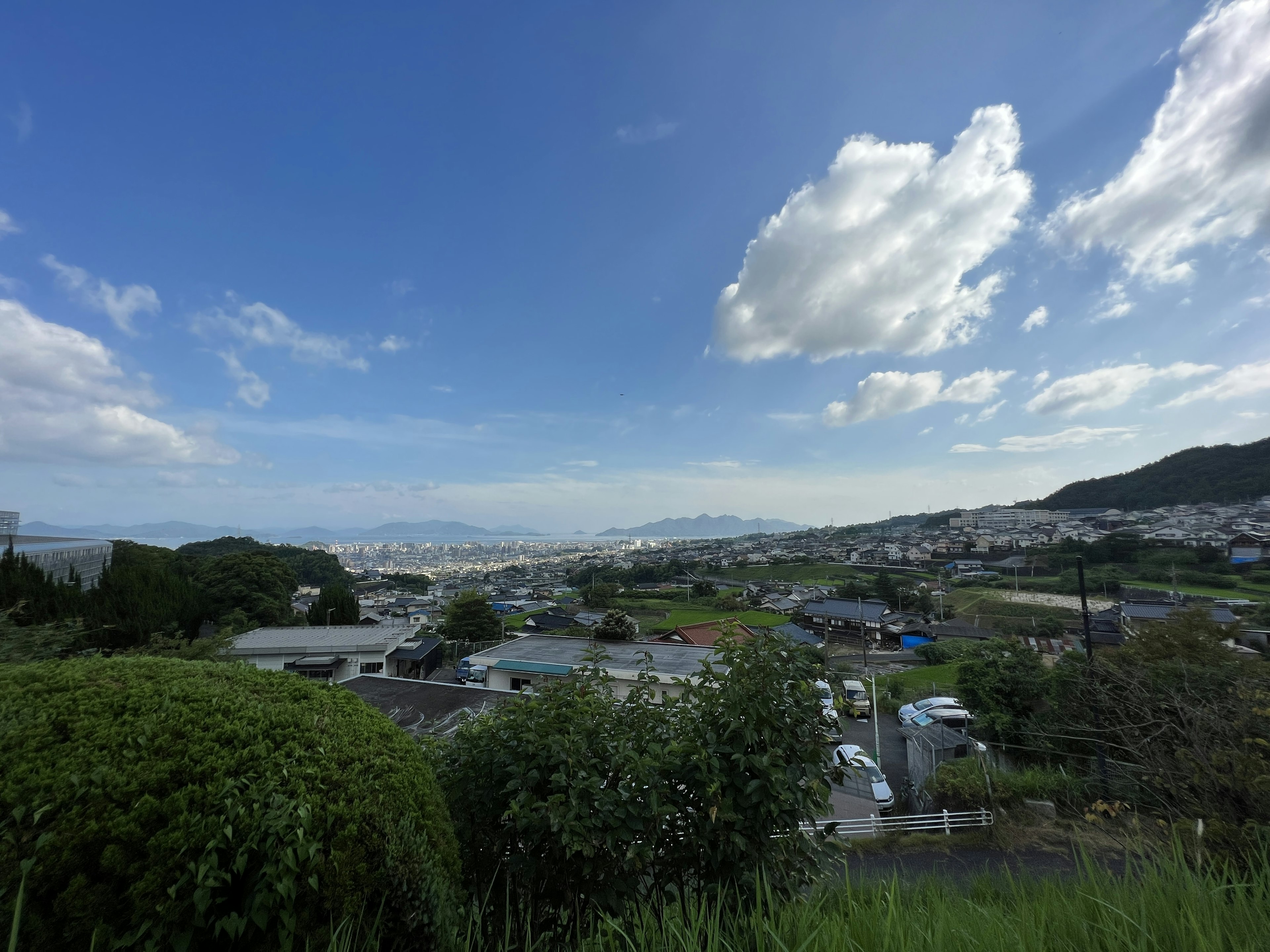 Paysage urbain sous un ciel bleu avec des nuages blancs végétation verte et montagnes lointaines