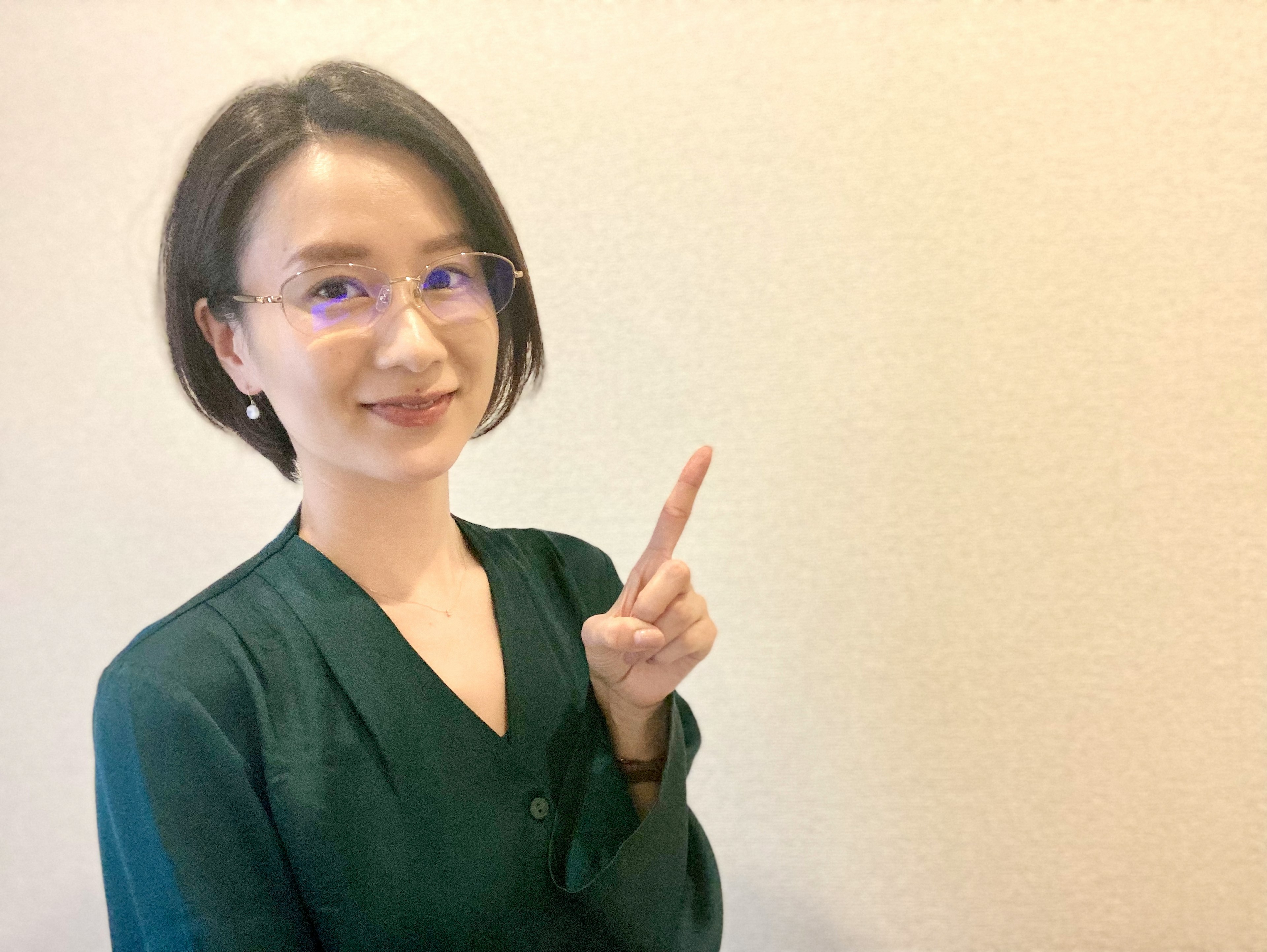 A woman in a green blouse smiling and pointing with one hand