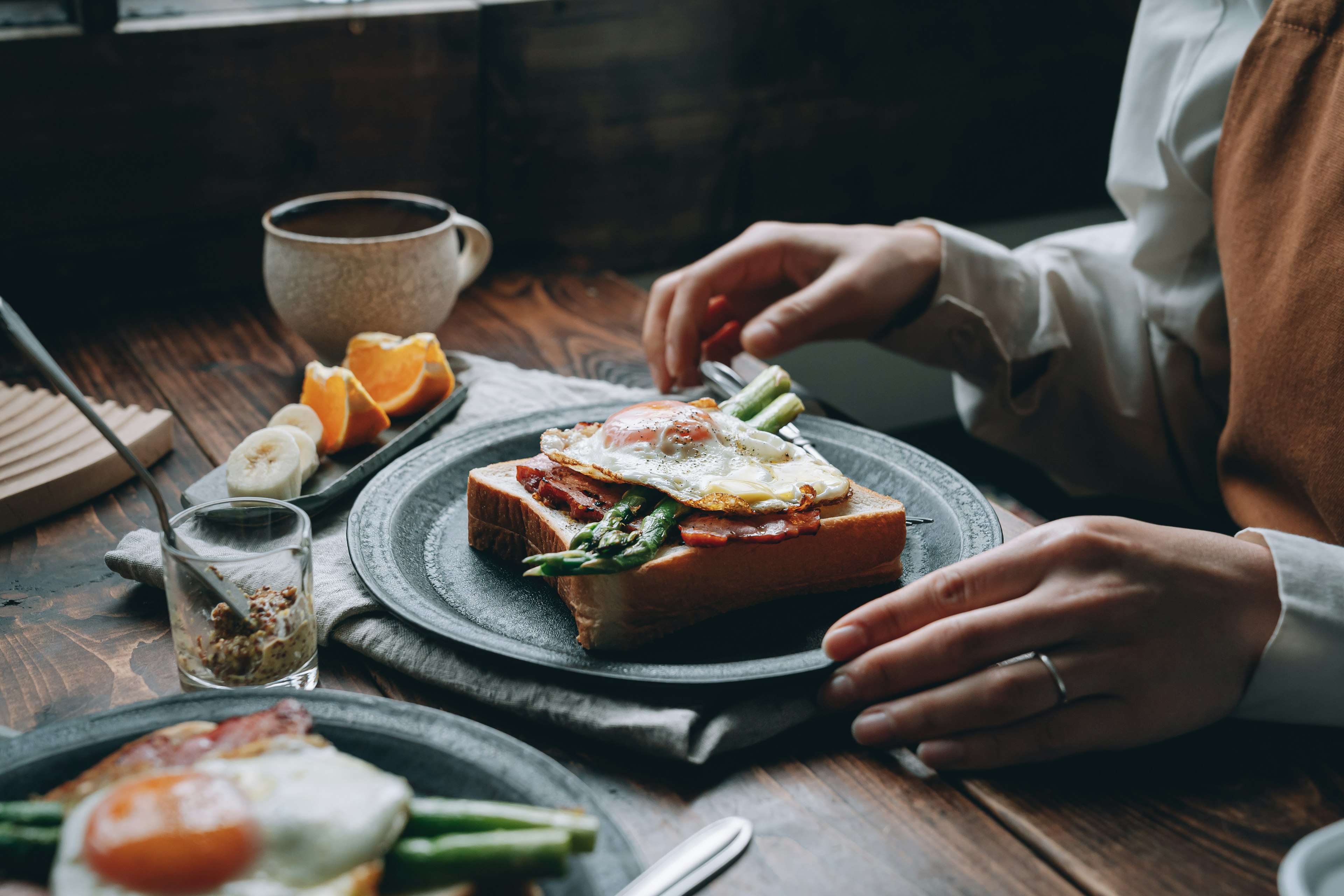 Gros plan sur une main préparant un toast au petit-déjeuner garni d'œuf et de légumes