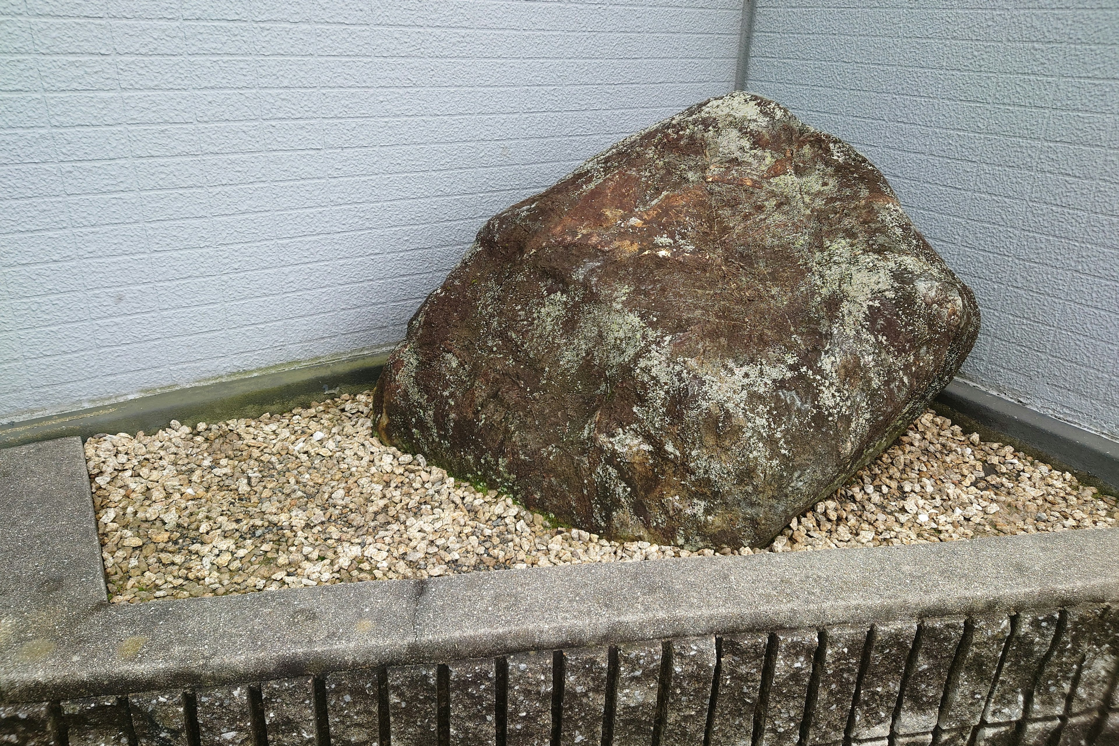 A large rock placed on small pebbles in a simple garden setting