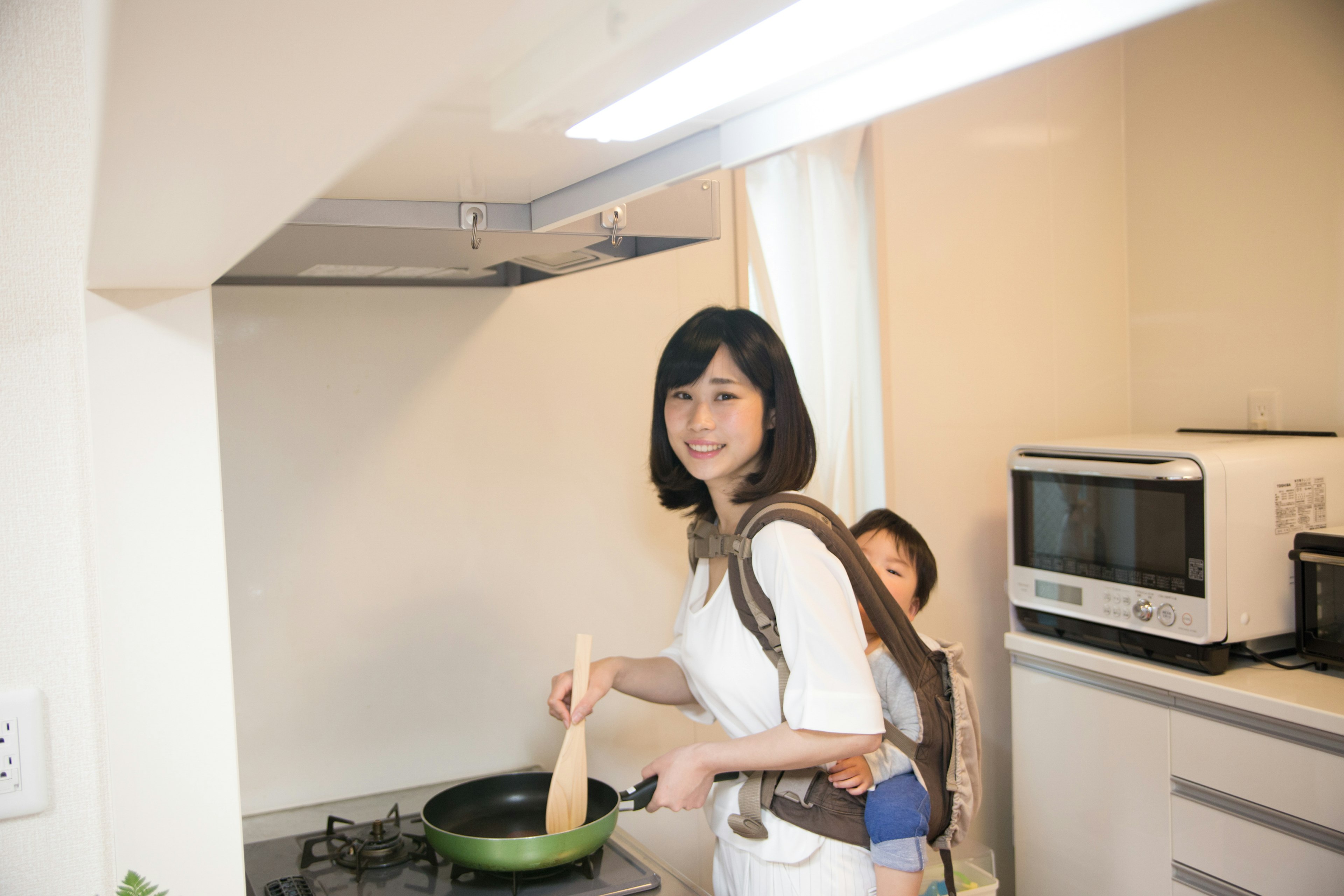 母親が子供を背負いながら料理をしているキッチンの風景