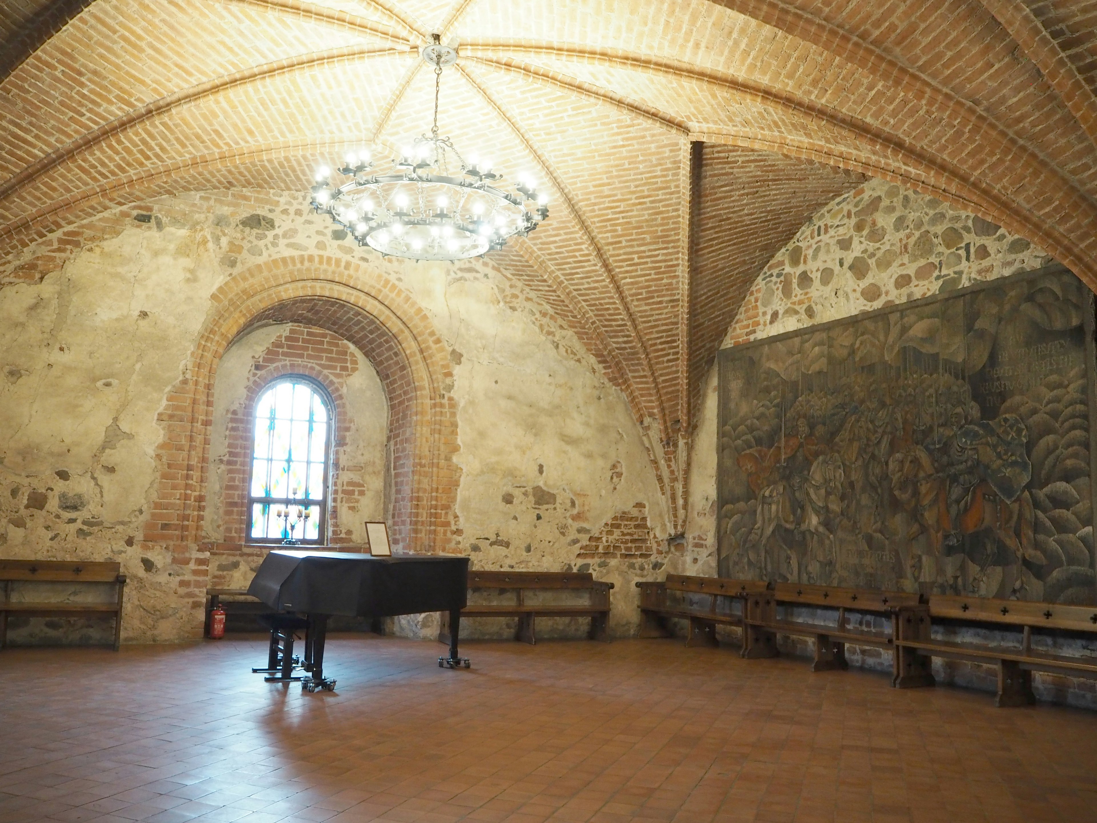 Spacious room featuring a black grand piano and an elegant chandelier in a historic setting