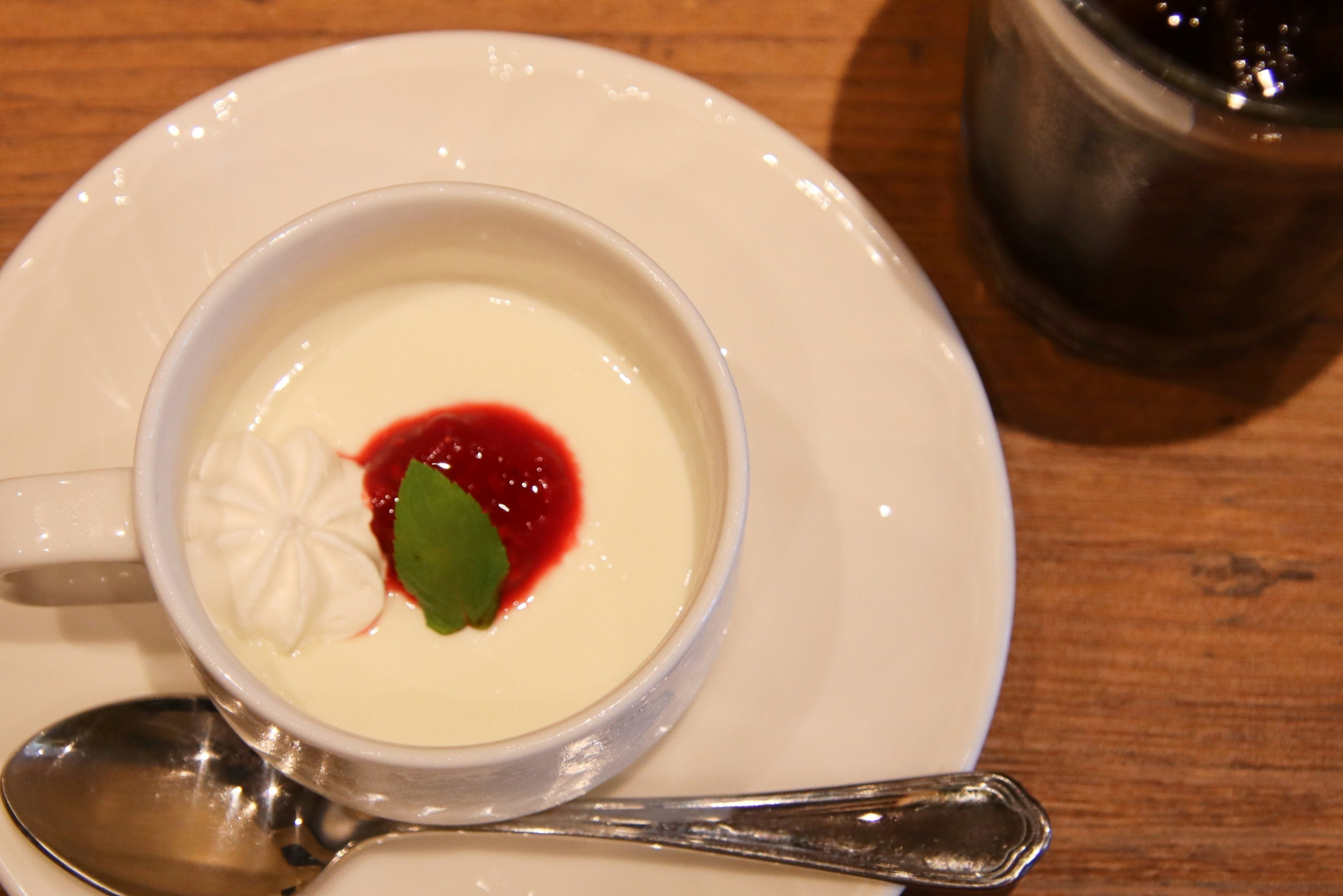 Postre cremoso en una taza blanca cubierto con salsa roja y una hoja de menta