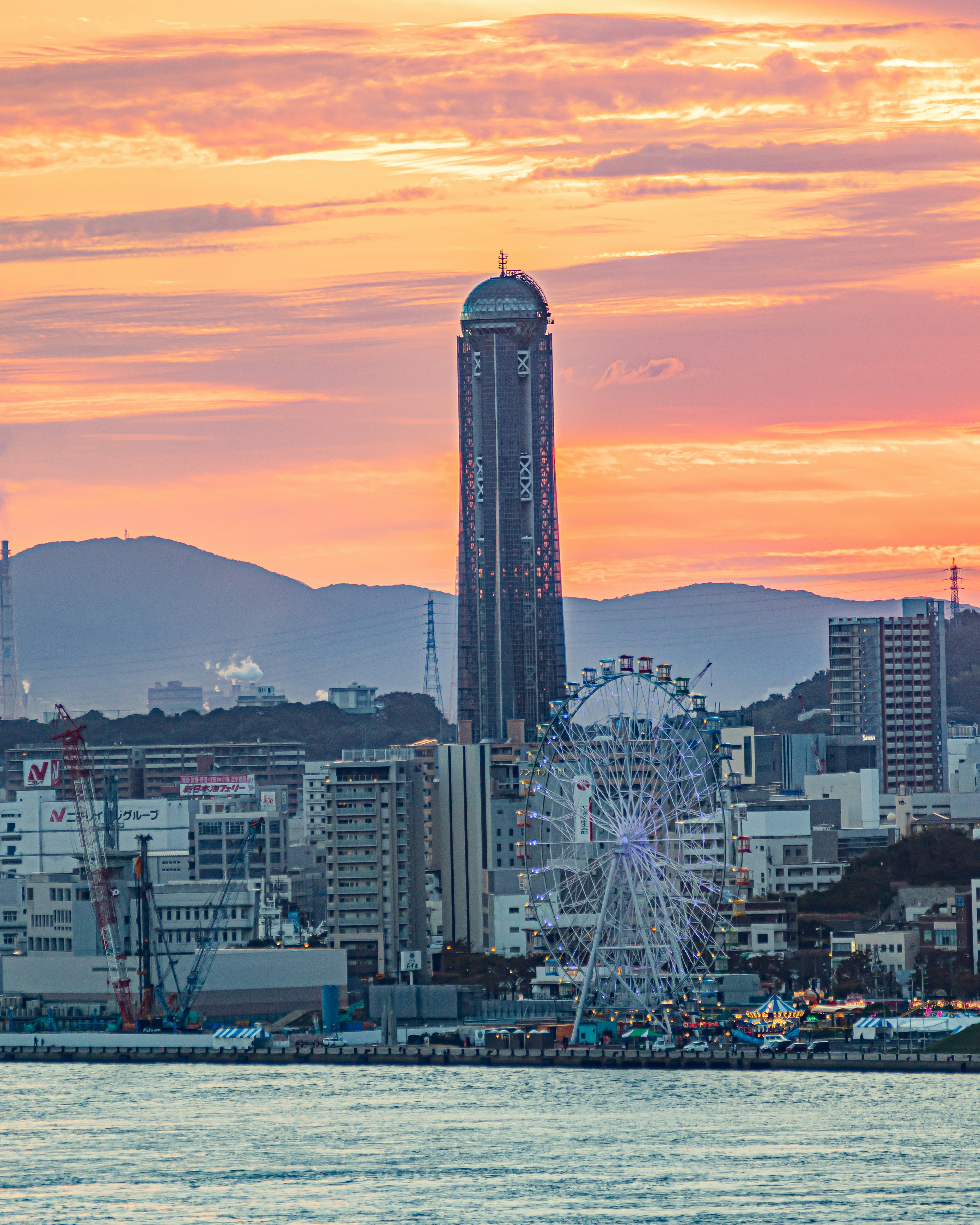 Paisaje urbano con un edificio alto y una noria al atardecer