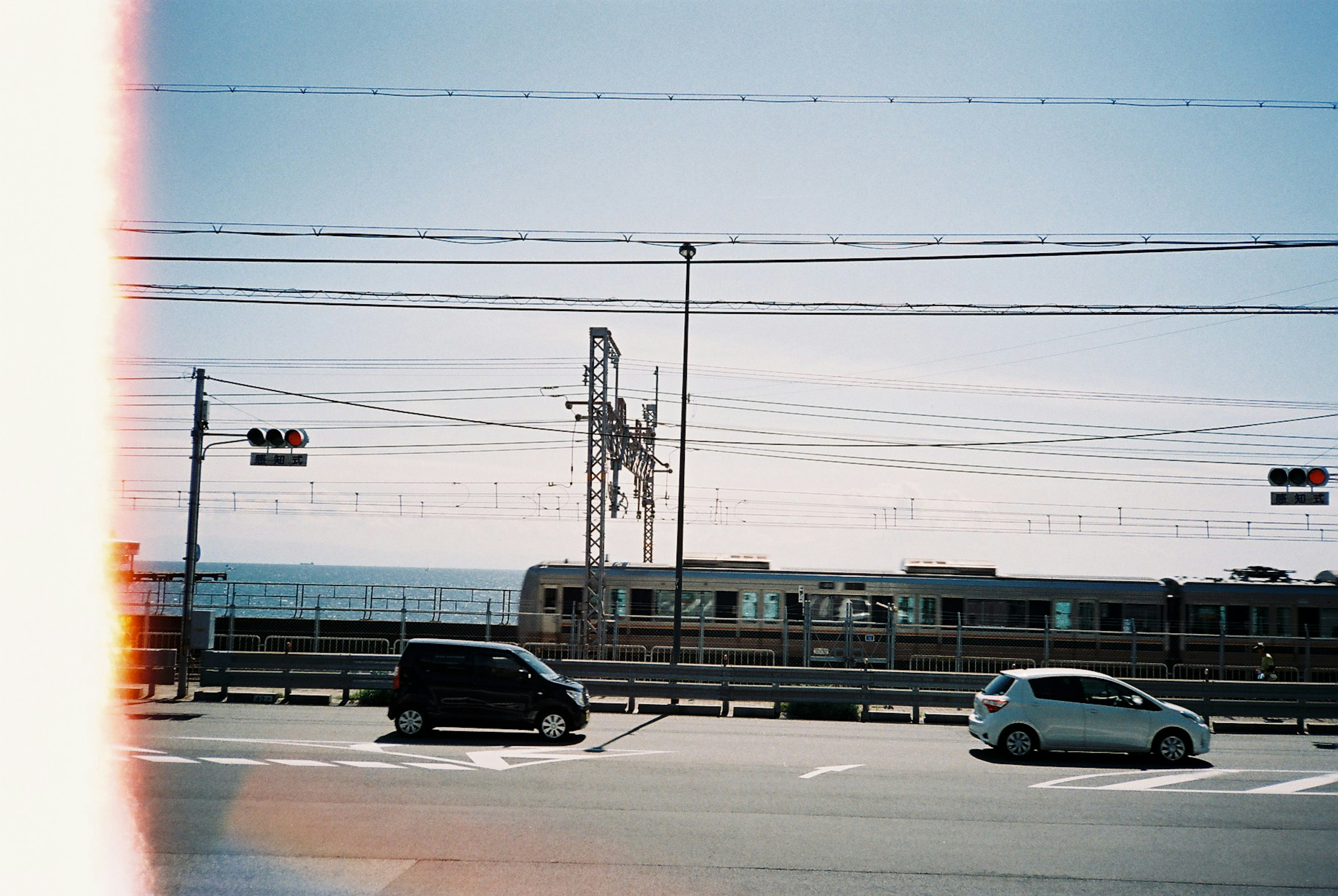 海の近くの道路に停車している黒い車と白い車の風景