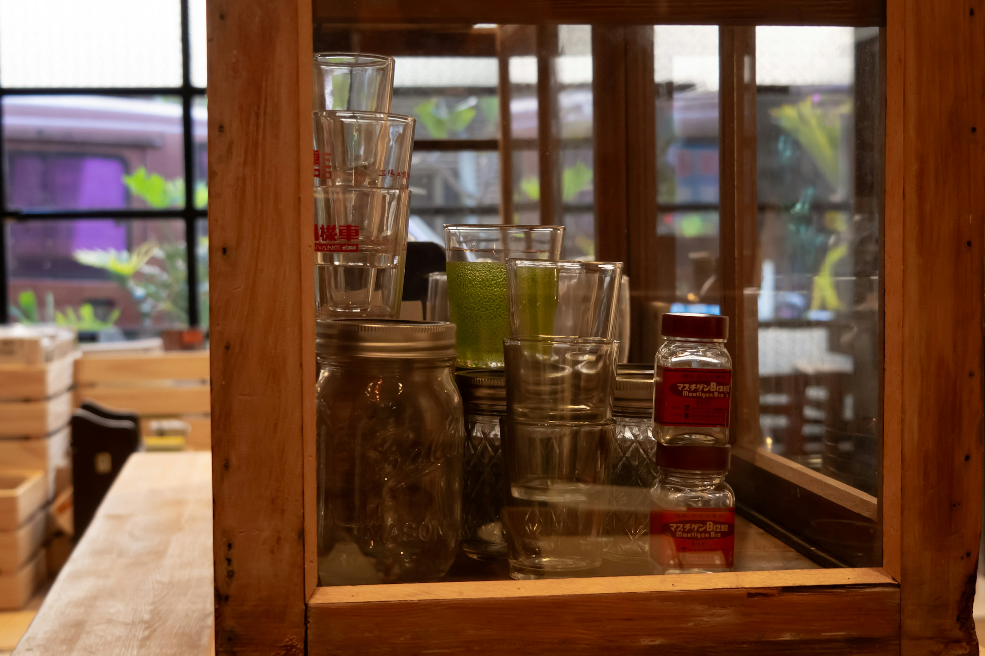 Collection of glass jars and cups arranged in a wooden cabinet