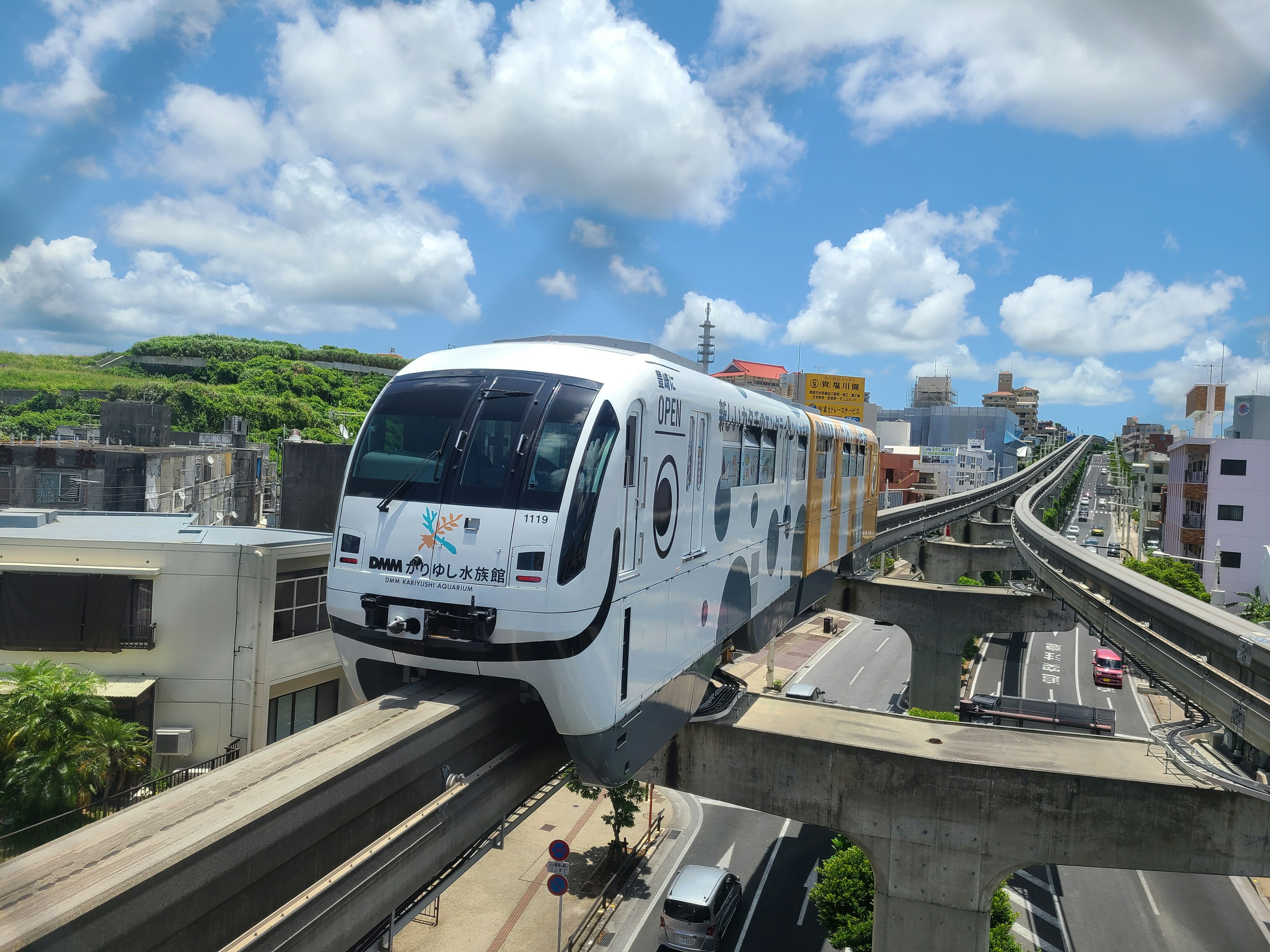 White monorail running above a city under a blue sky with white clouds