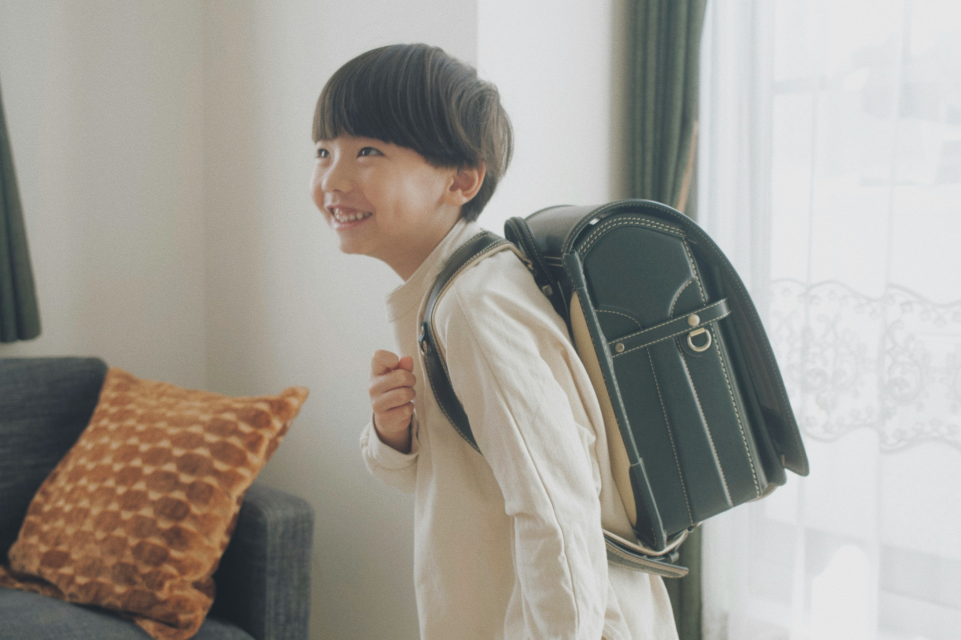 A child smiling while wearing a green backpack in a bright indoor setting