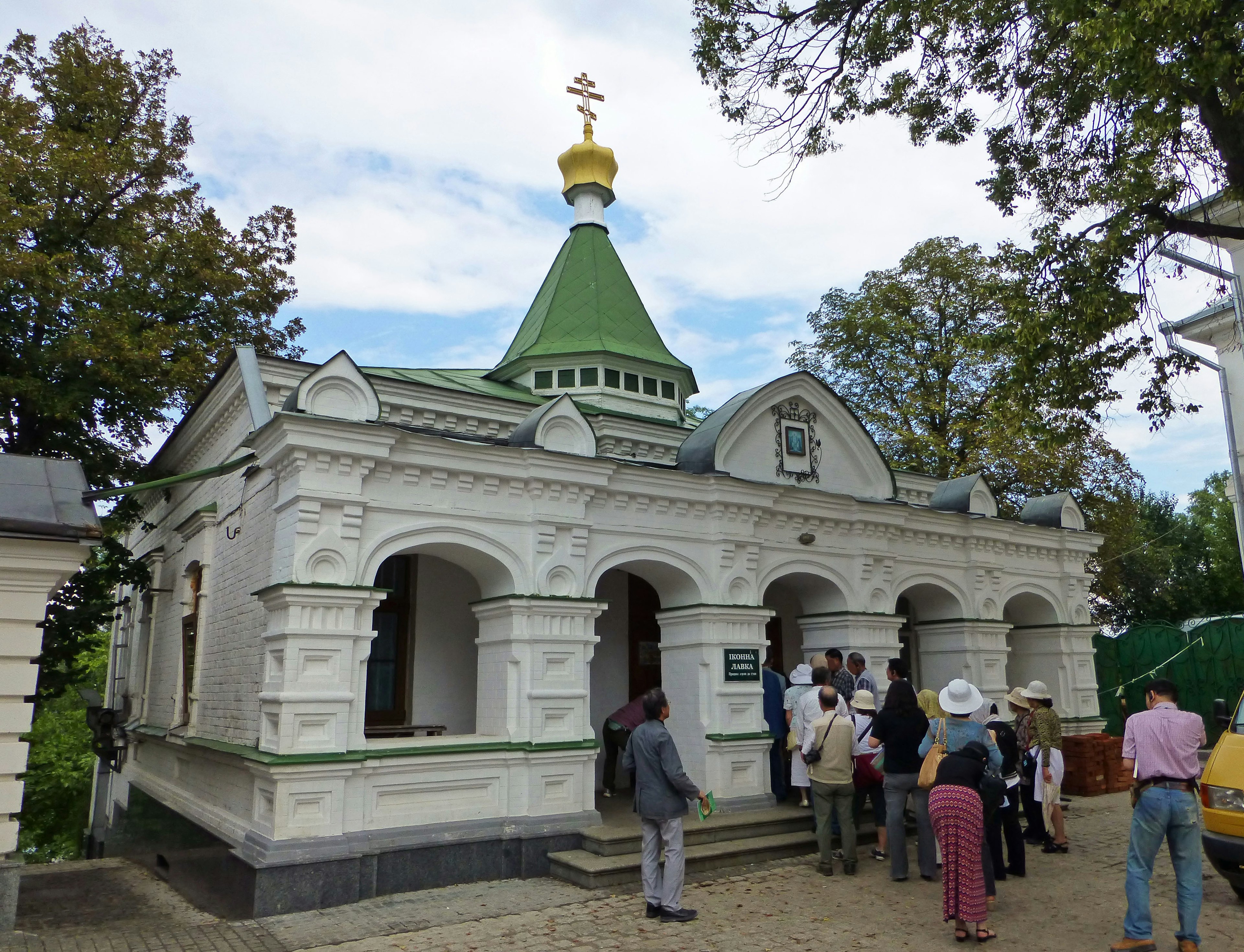 Extérieur d'une église blanche avec un toit vert et une croix dorée de nombreuses personnes en visite