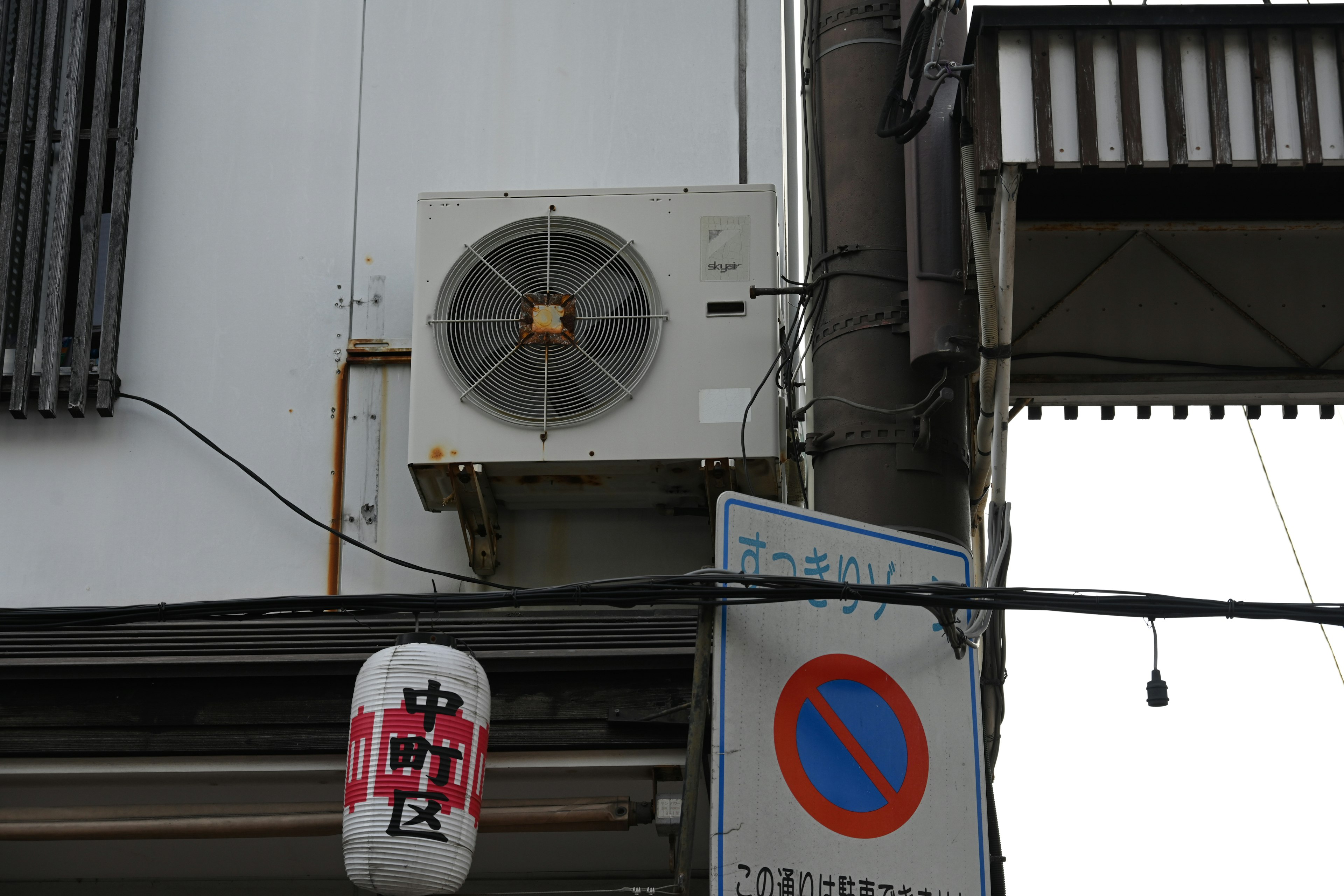 Street corner scene featuring a wall-mounted air conditioner and a red lantern