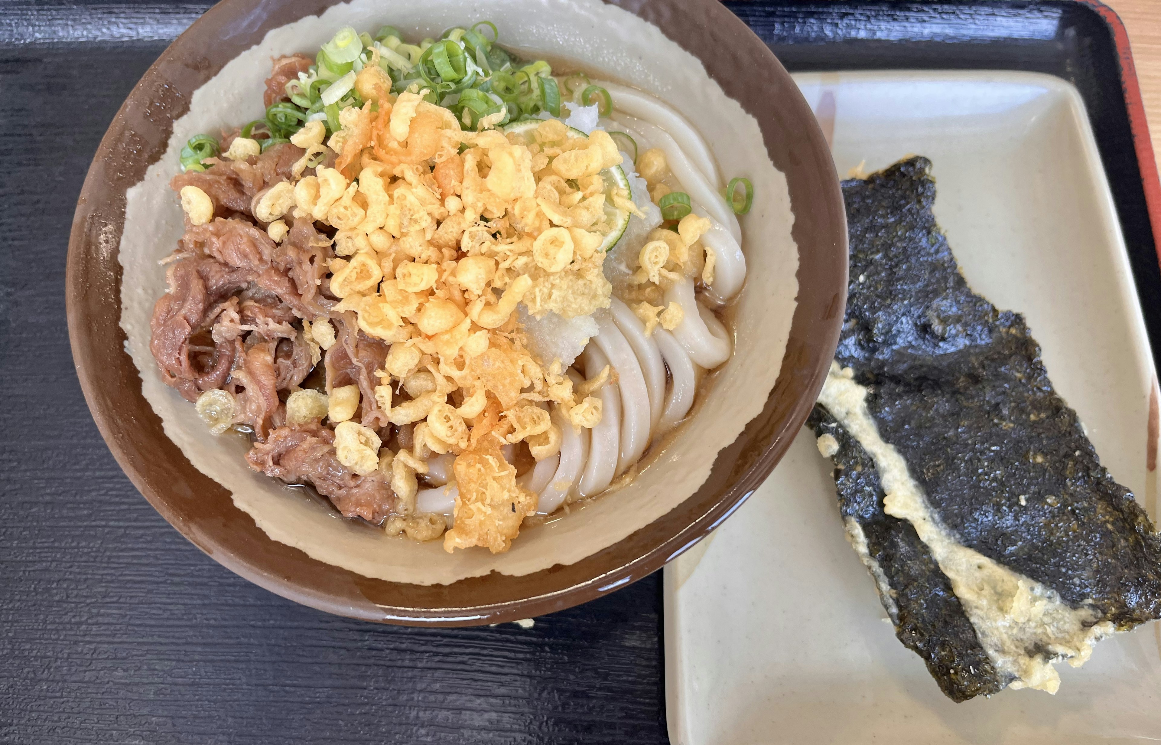 Bol de udon avec du bœuf garni de flocons de tempura frits et d'oignons verts