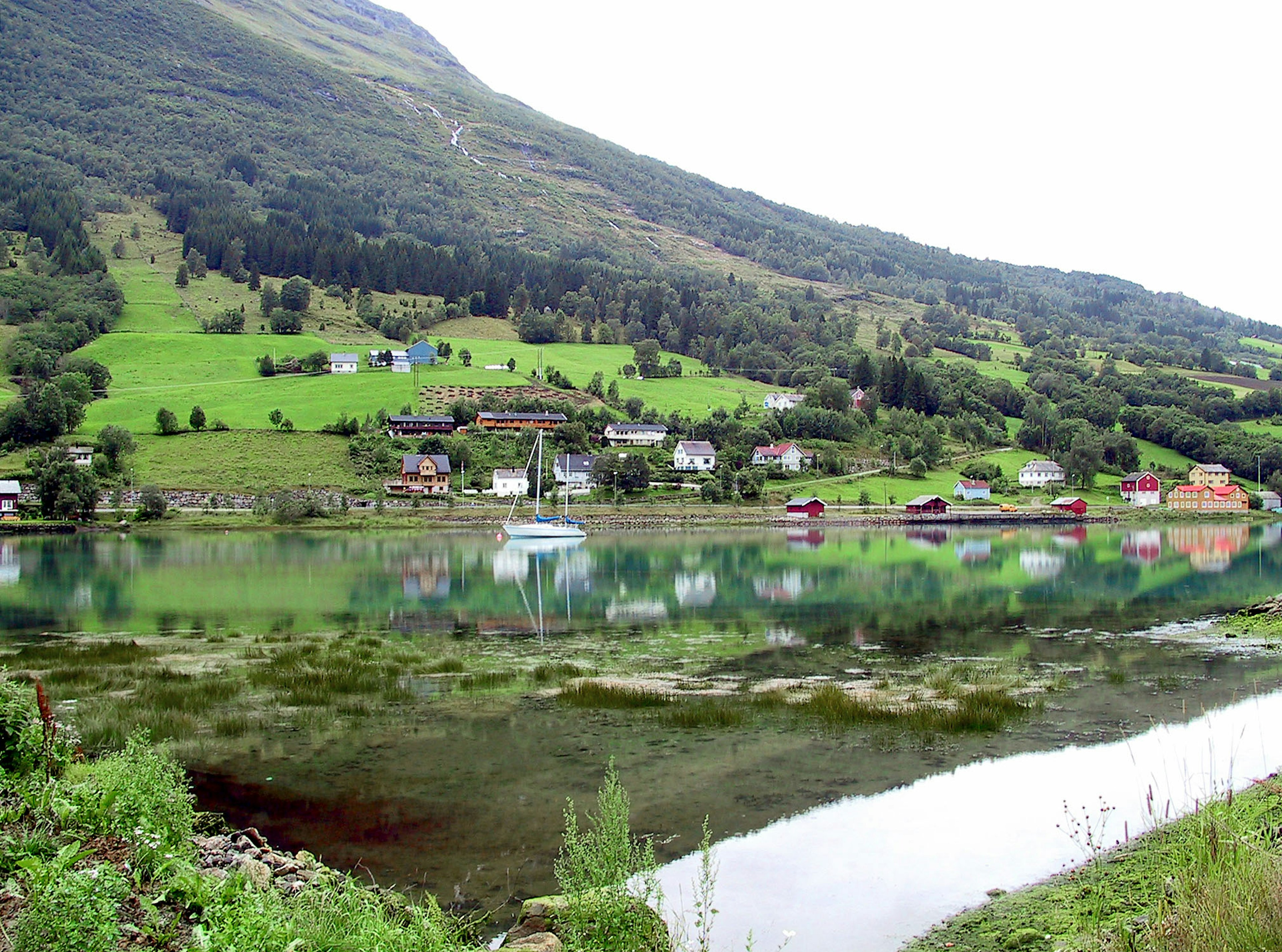 Vista panoramica di montagne verdi e lago tranquillo che riflette case e natura