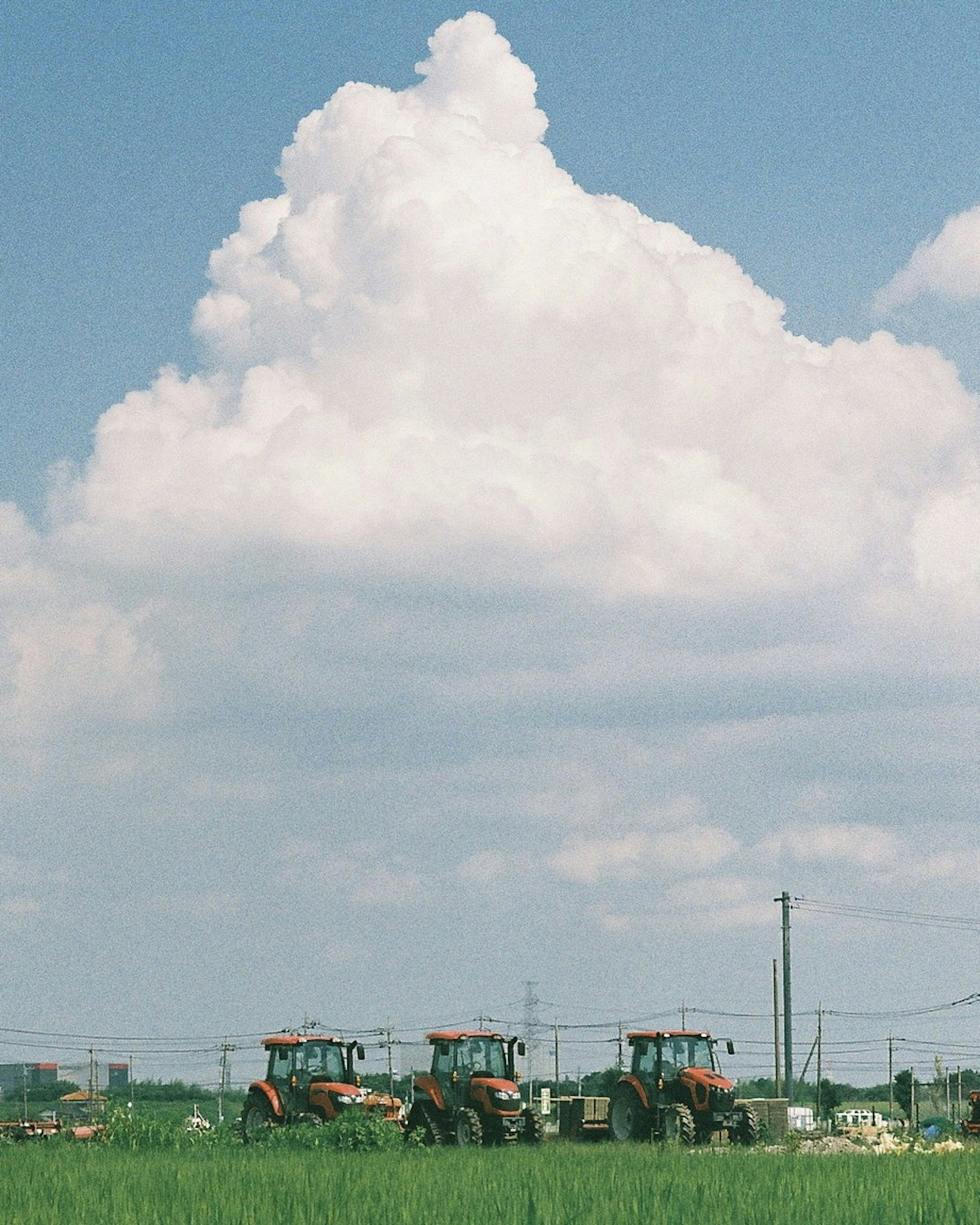 Tractors working in a green field under a large fluffy cloud