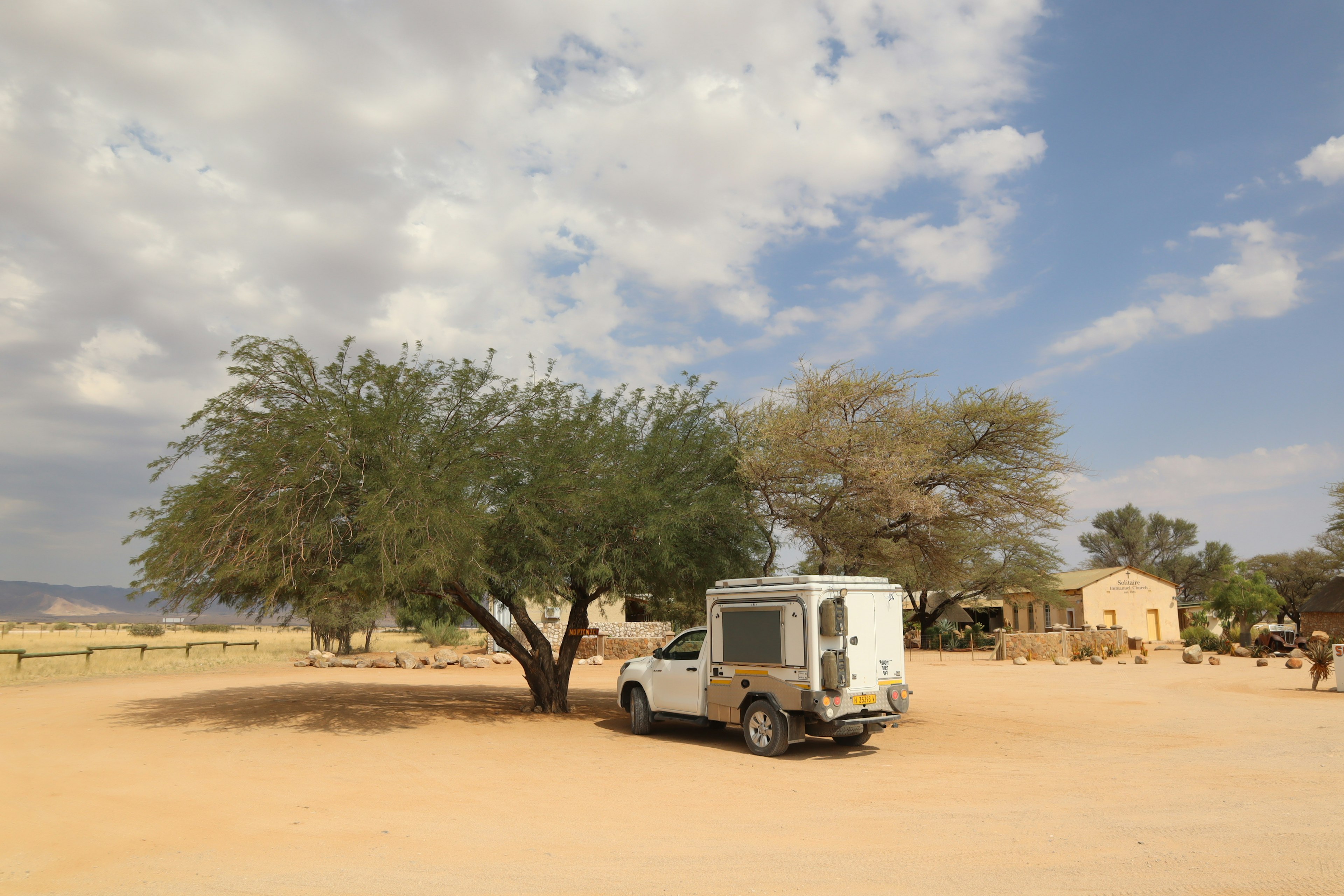 Un camper parcheggiato sotto un grande albero con un paesaggio secco sullo sfondo