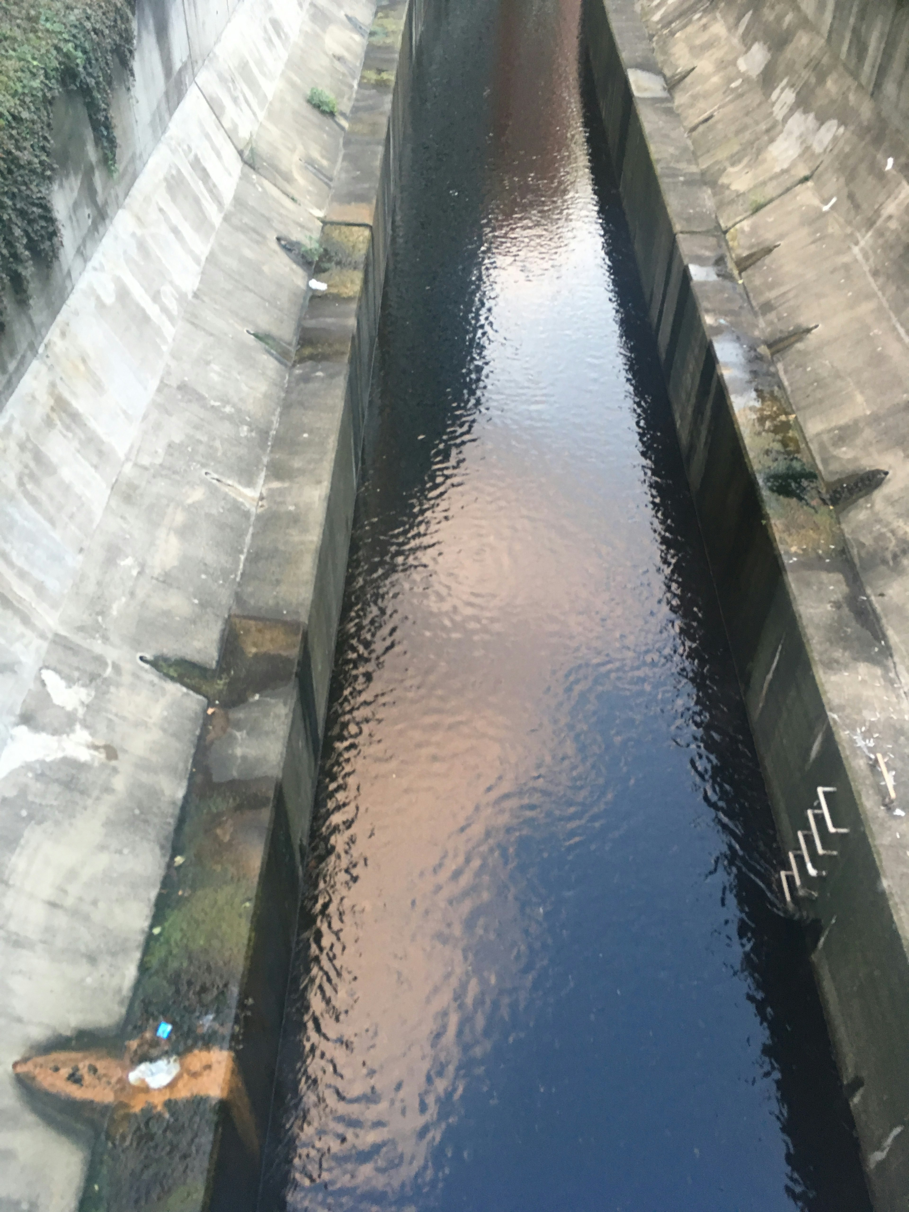 Vue d'un canal sombre avec de l'eau qui s'écoule vu d'en haut murs en béton fissurés et reflets sur la surface de l'eau