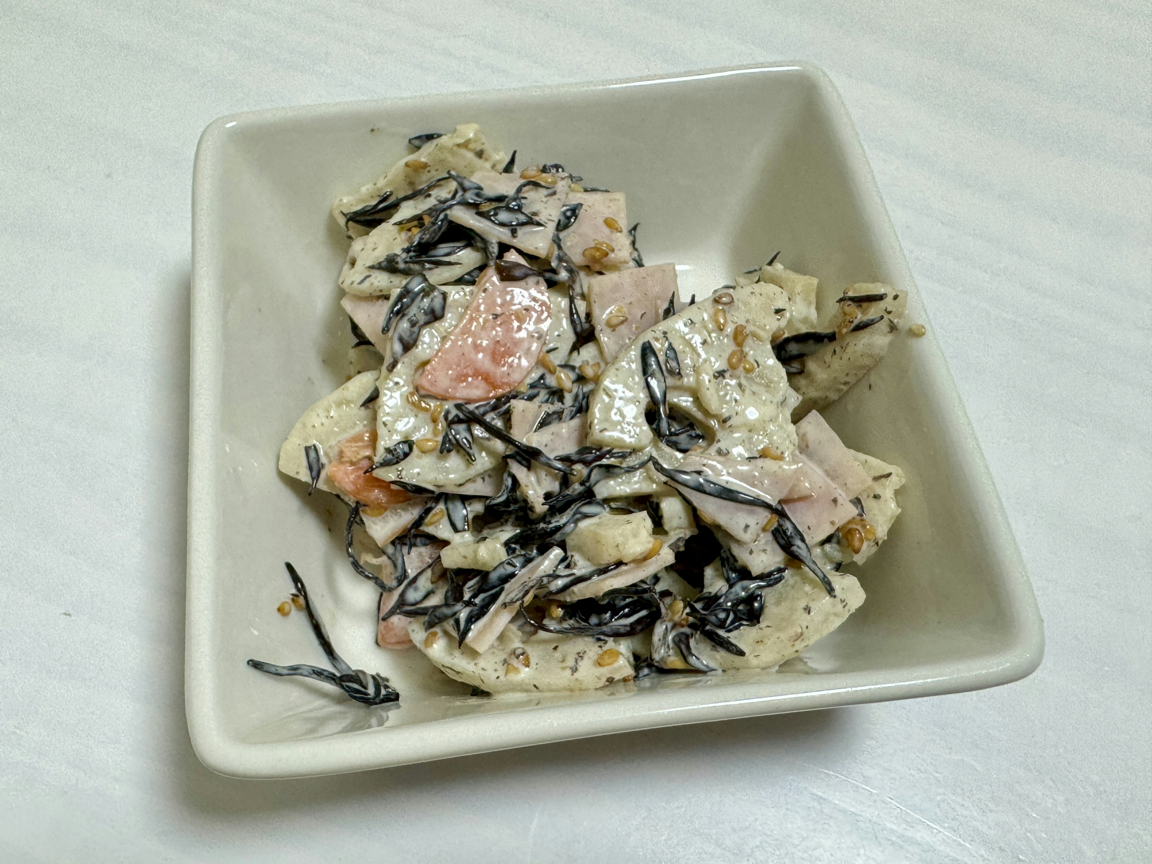 A salad with hijiki seaweed and salmon served in a white bowl