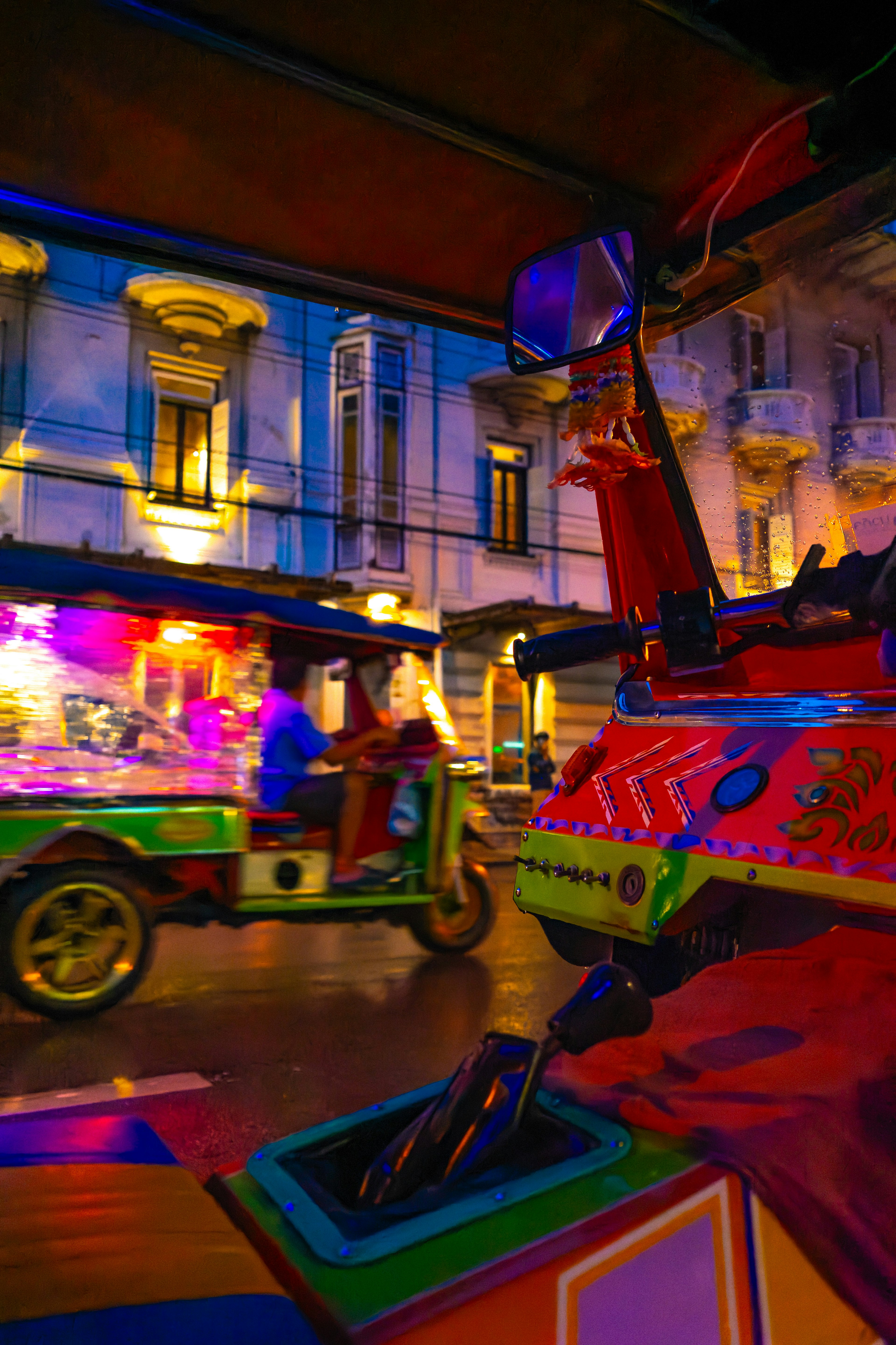 Tuk-tuks coloridos pasando por un paisaje urbano vibrante de noche