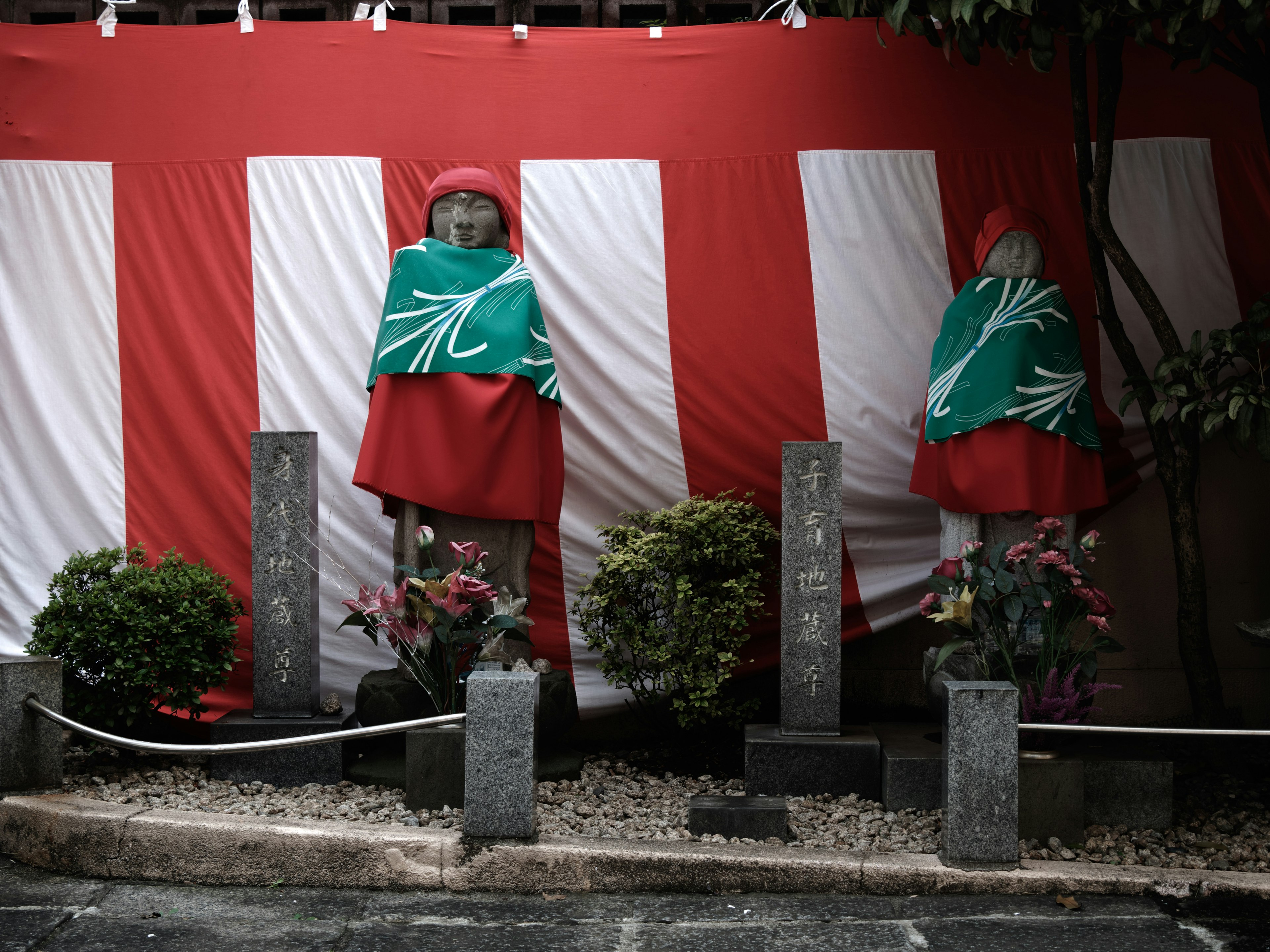 Two statues wearing green capes in front of a red striped backdrop with stone monuments