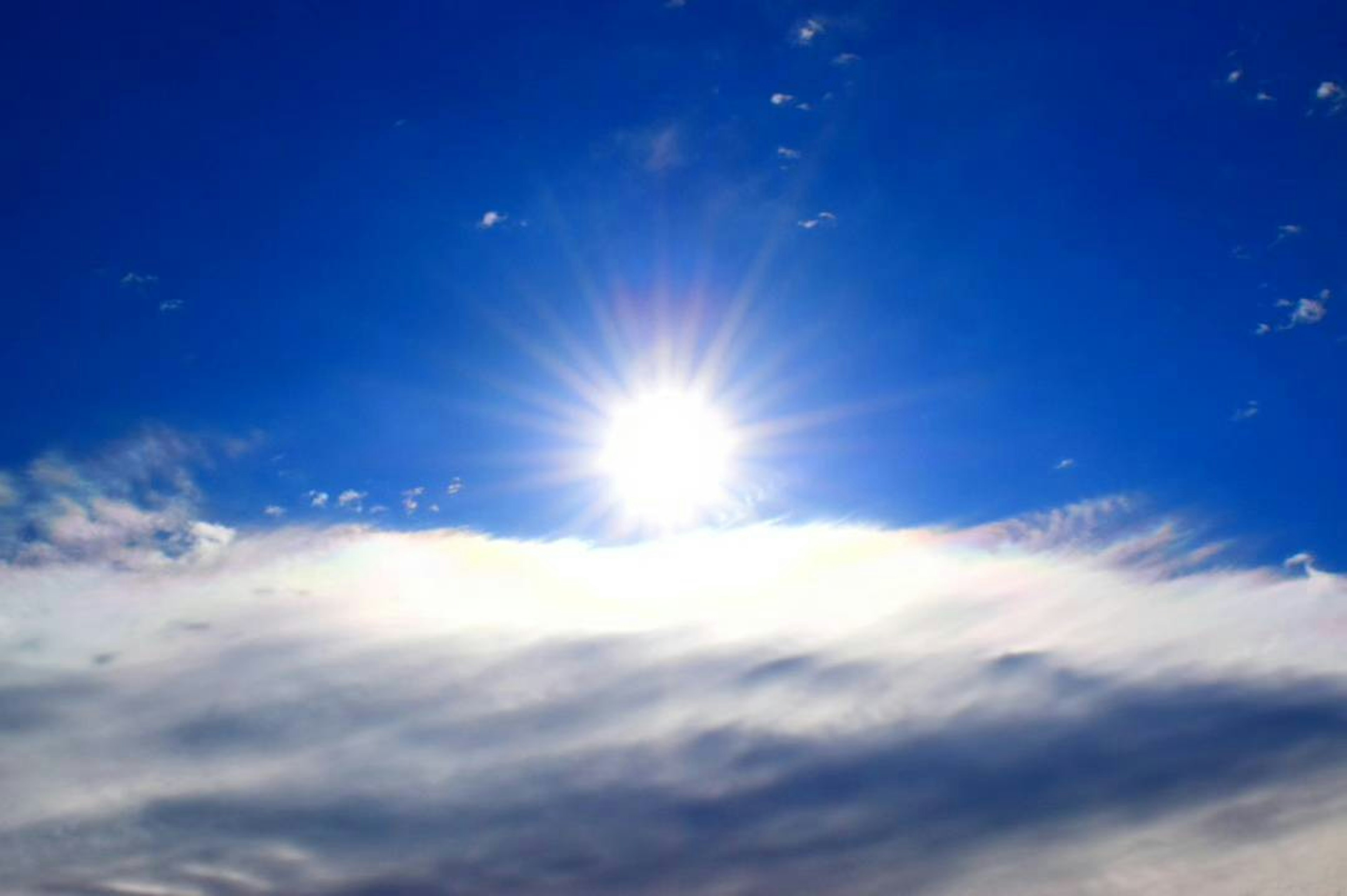 Bright sun shining above clouds in a clear blue sky