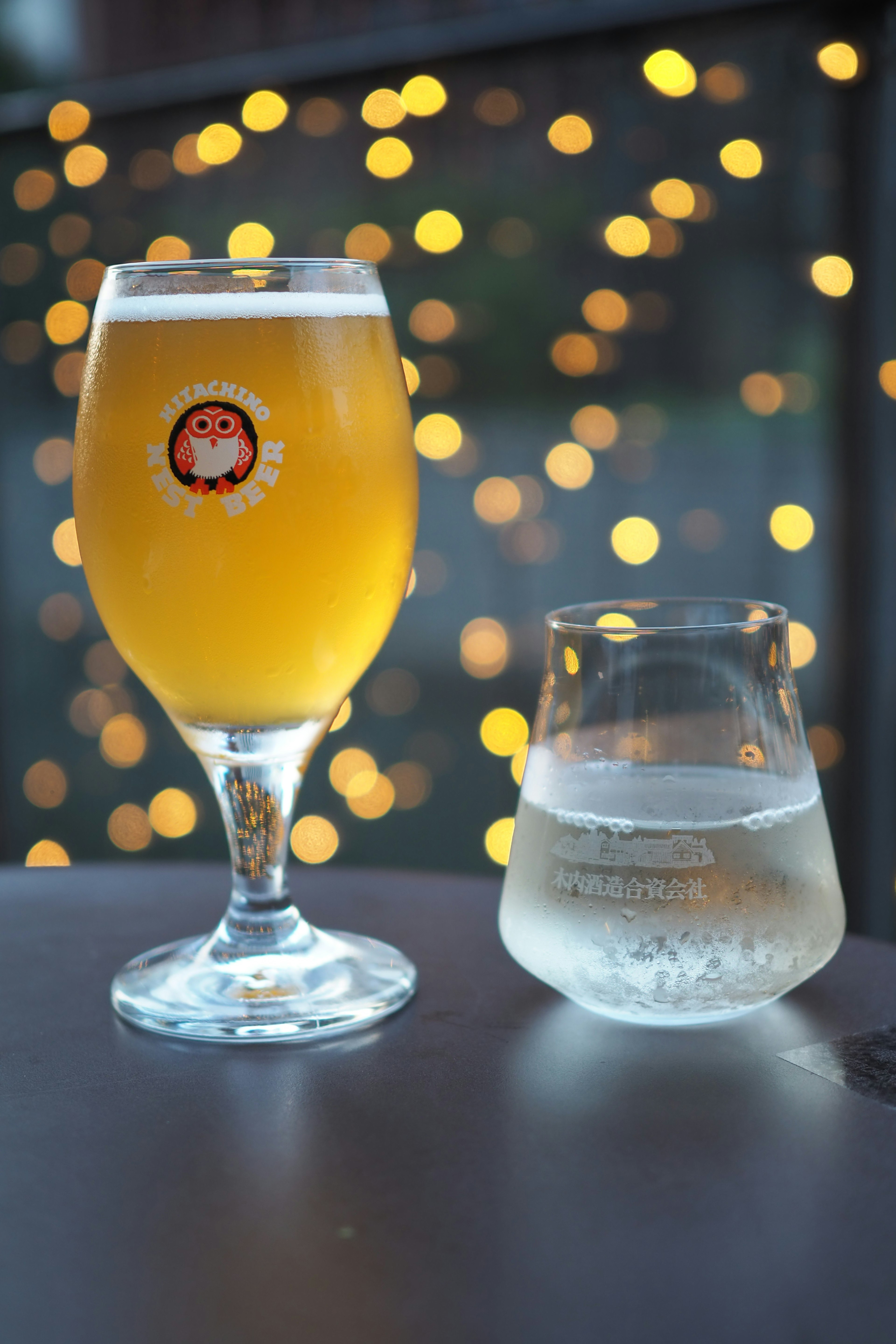 Un vaso de cerveza y un vaso de agua sobre una mesa con luces bokeh al fondo