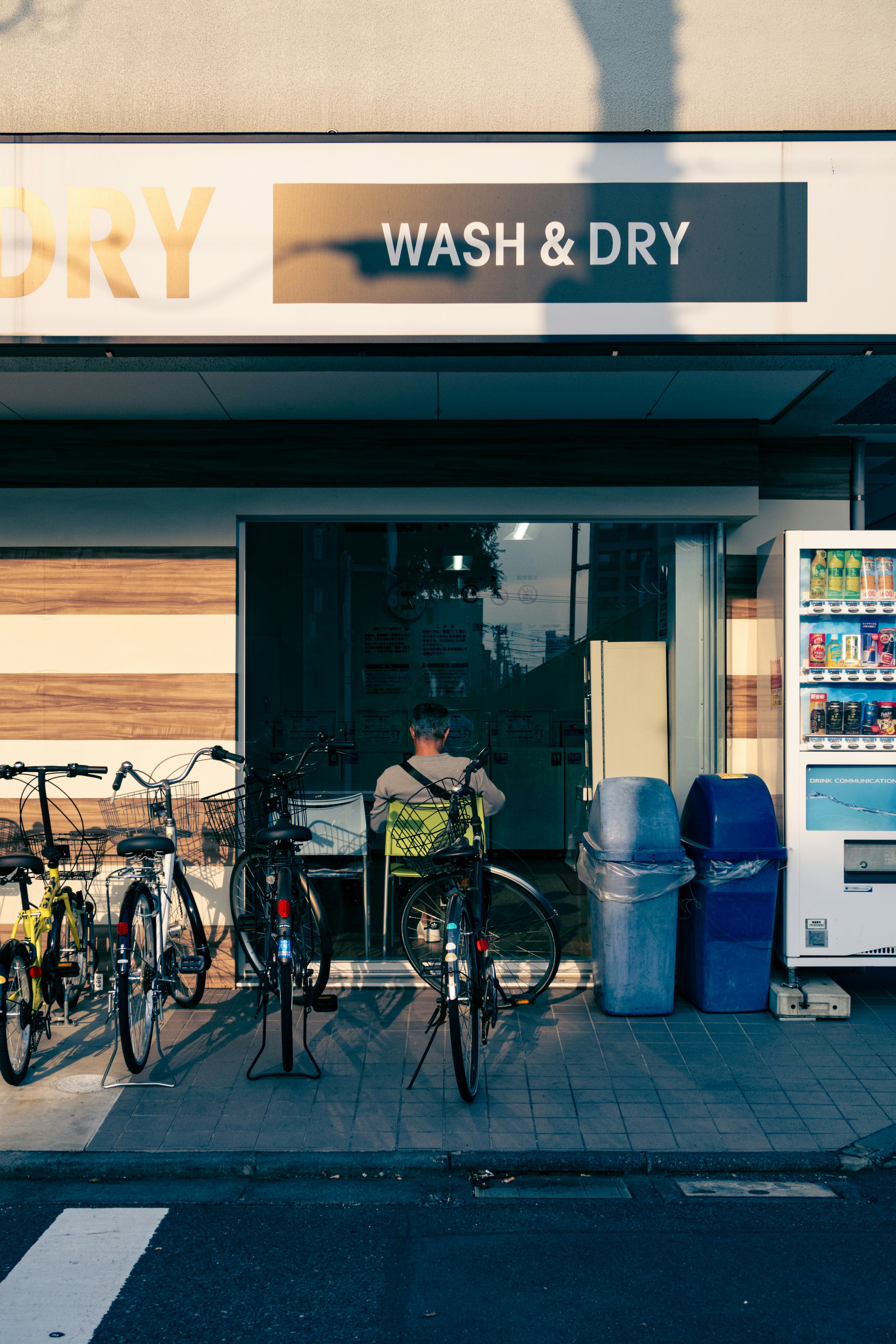 Person sitting outside a laundry shop with bicycles