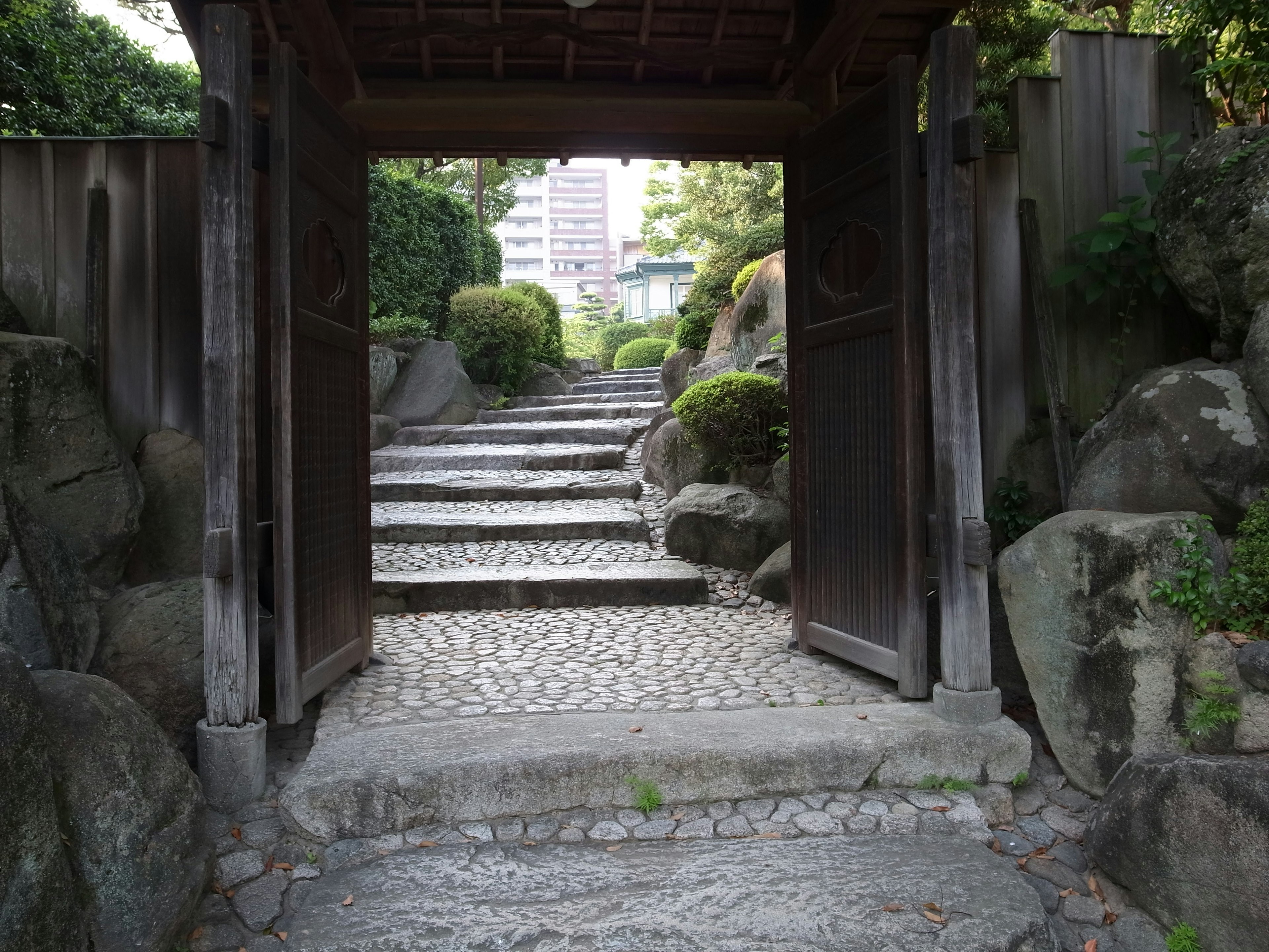 Entrée d'un jardin japonais avec des marches en pierre et une porte en bois