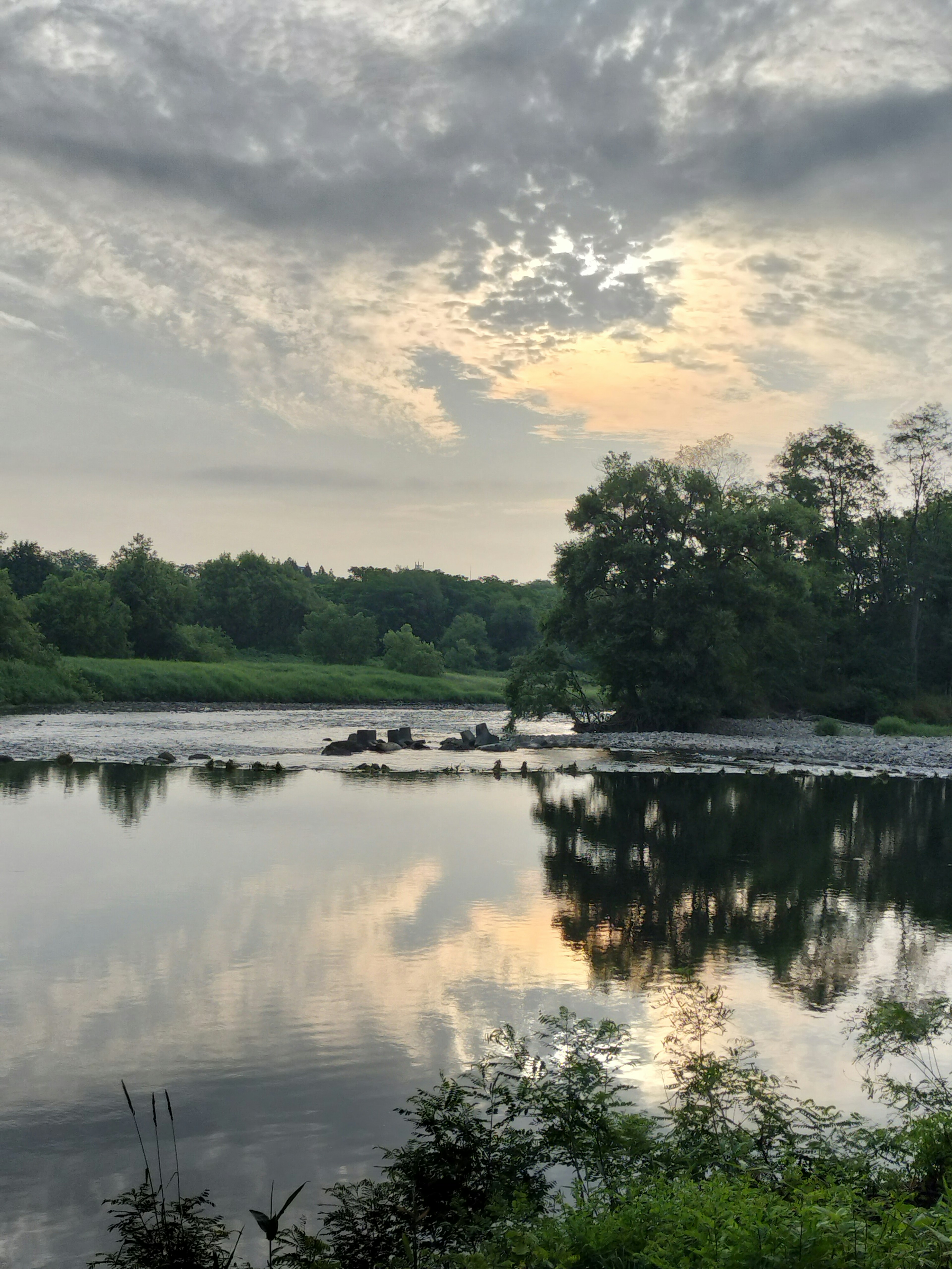 Danau tenang mencerminkan awan dan pepohonan