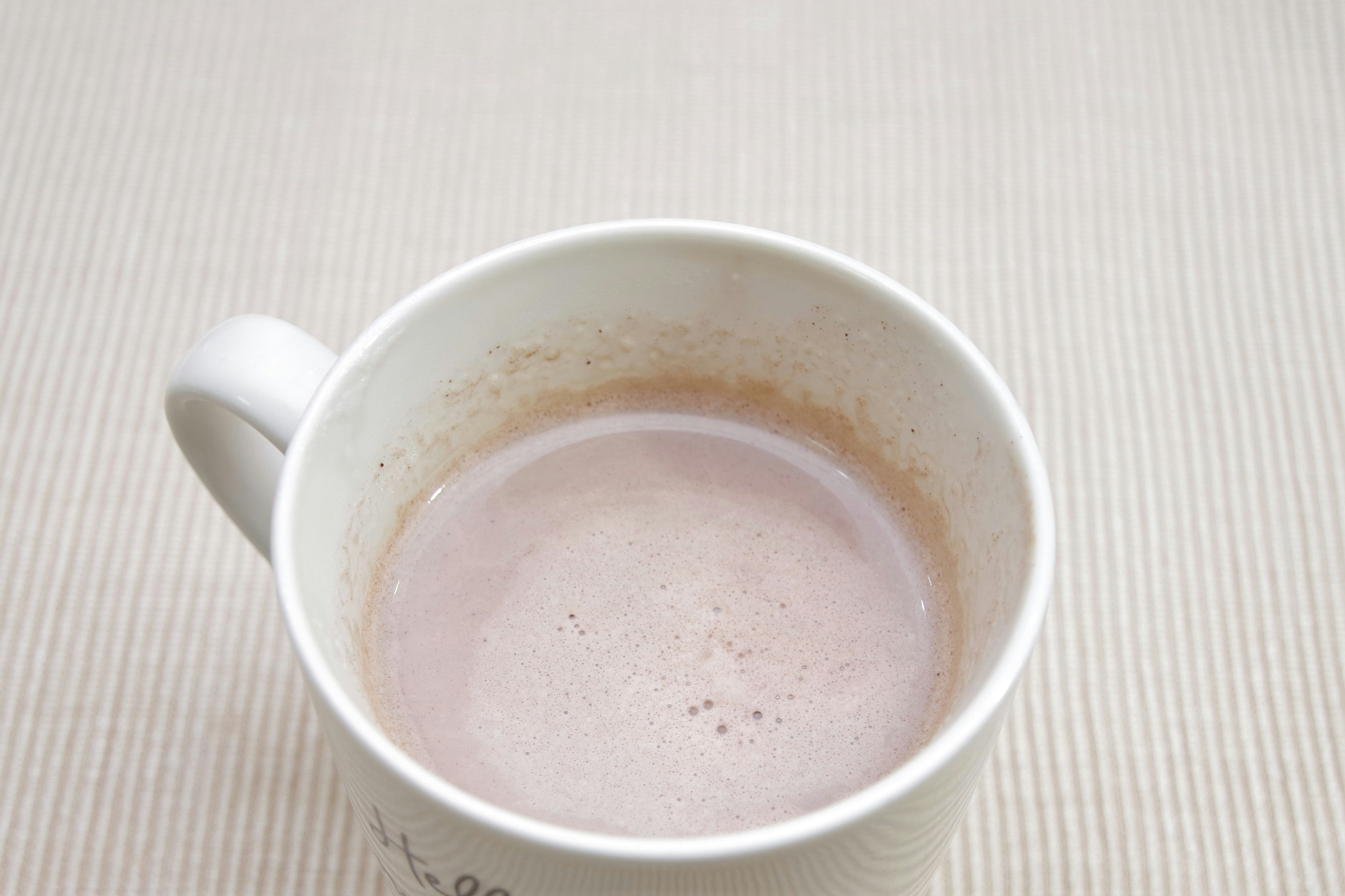 Une boisson brune claire avec de la mousse dans une tasse blanche